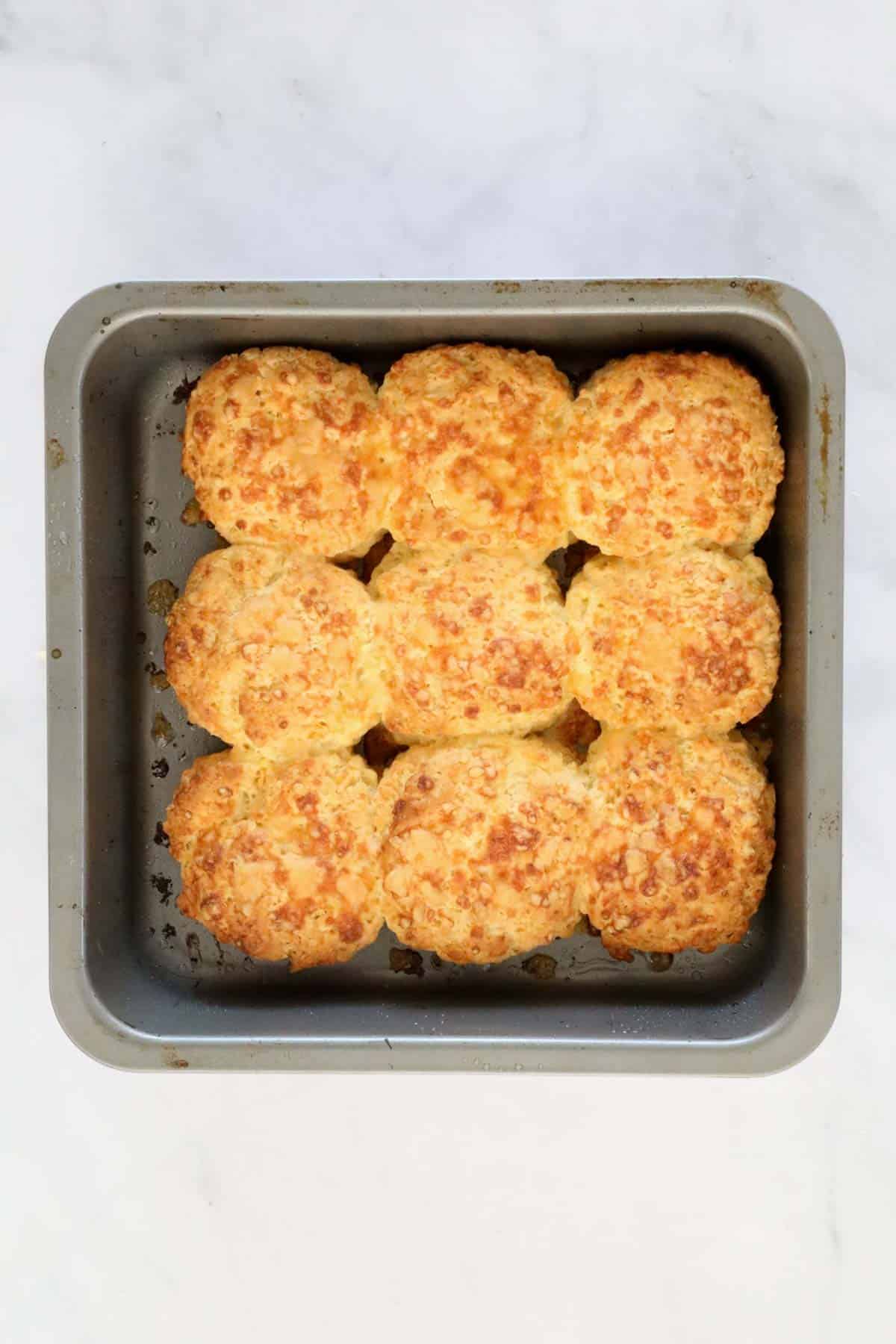 Baked scones with crispy baked cheese on top, in a square baking tin.