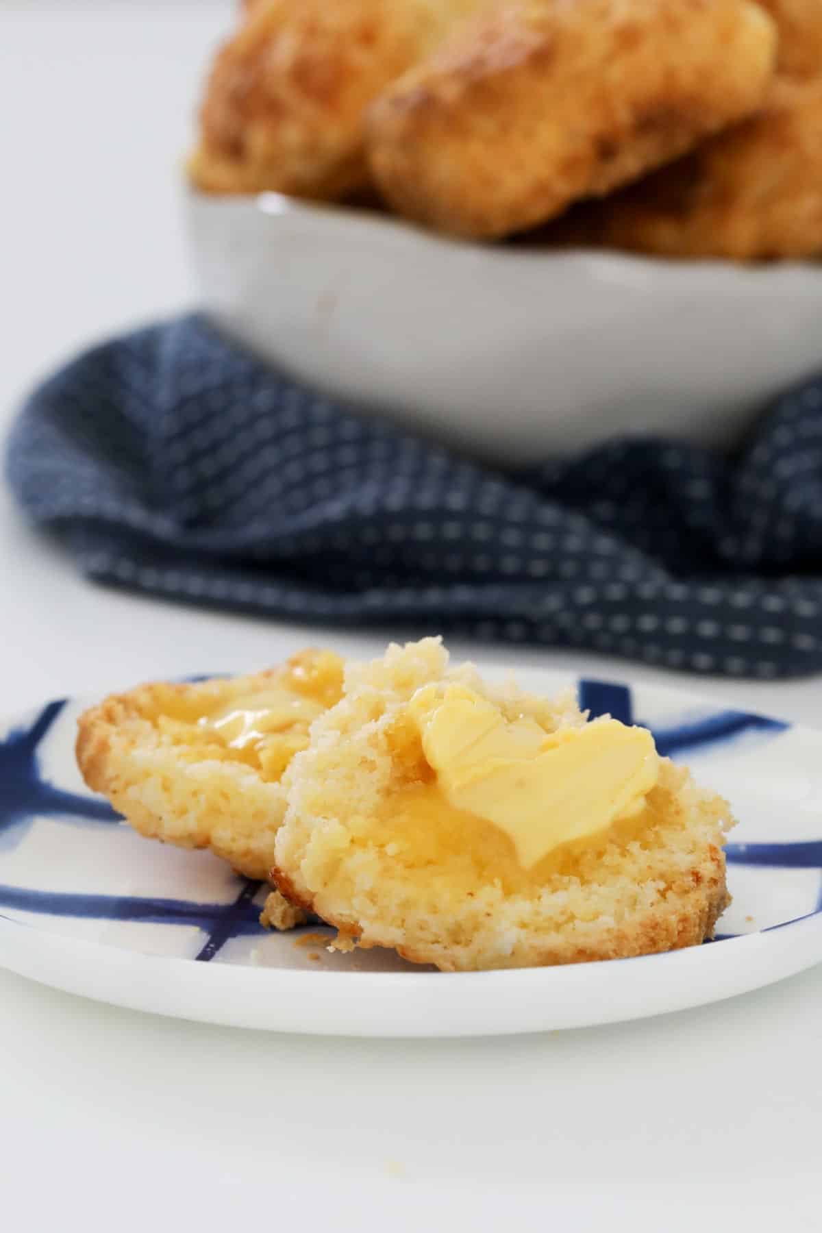 A gluten free cheese scone split and buttered, and served on a plate.