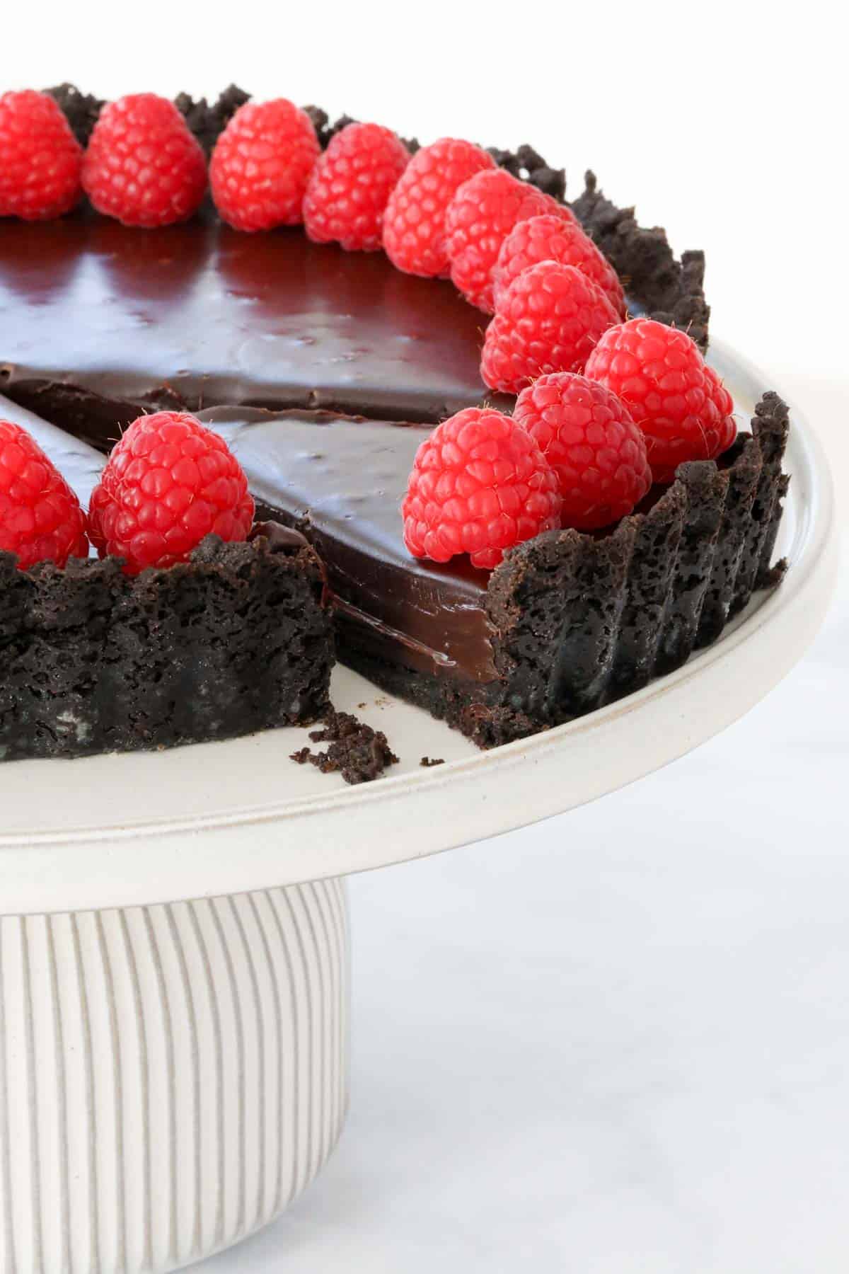 A chocolate tart decorated with raspberries with one slice partially removed.