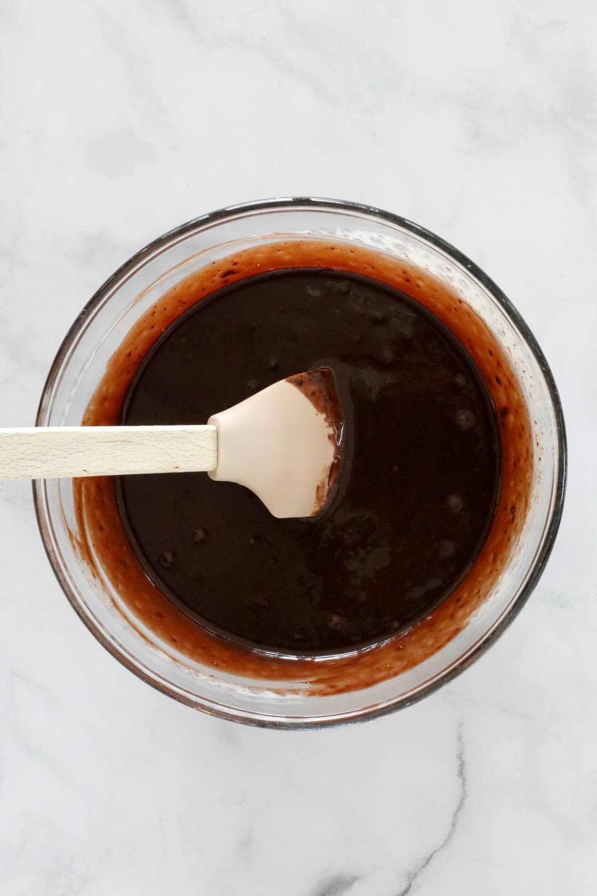Cream and melted chocolate stirred with a wooden spoon in a glass bowl.