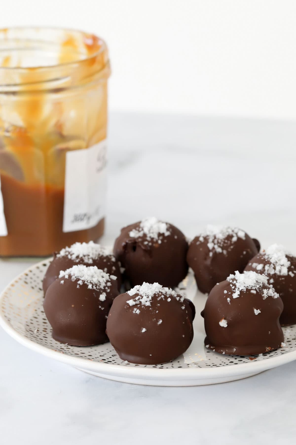 Side view of caramel truffles on a plate with a jar of caramel behind.