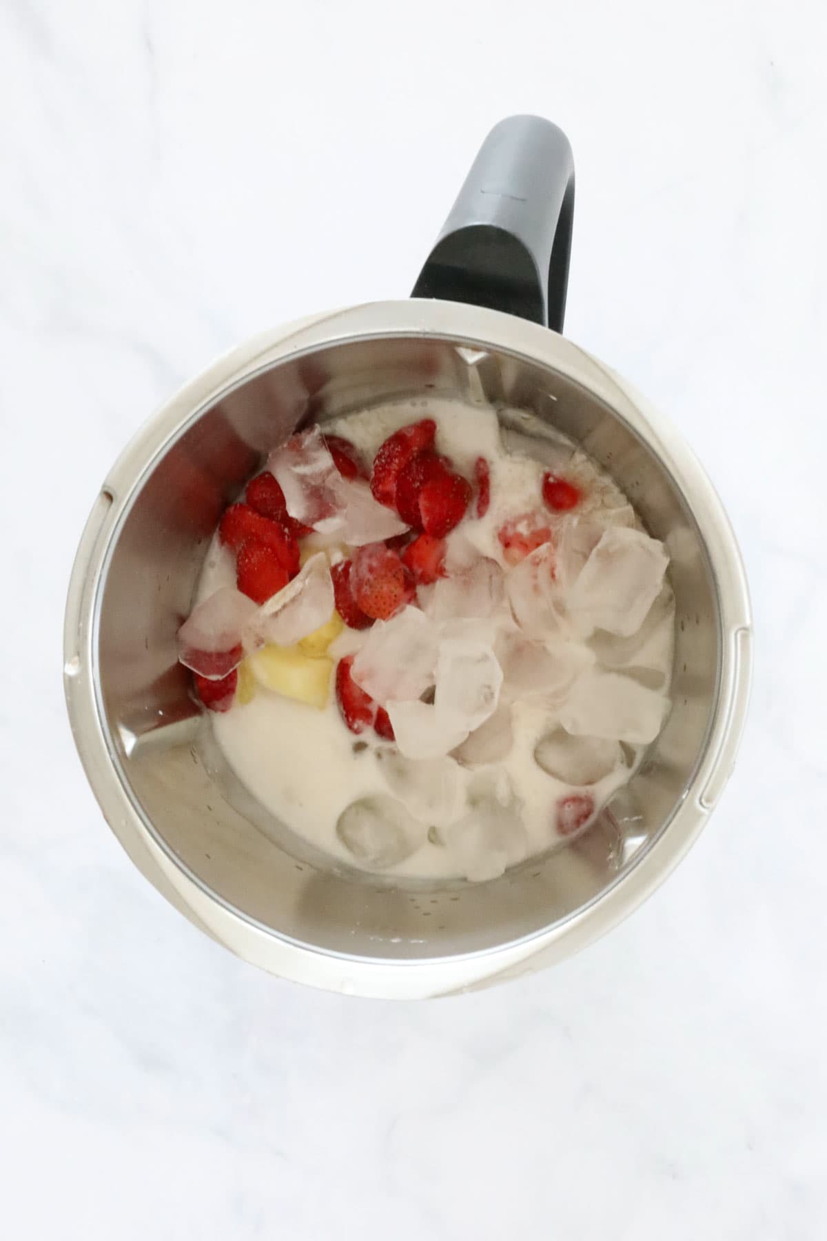 Ice, strawberries, pineapple and coconut cream in a blender jug.