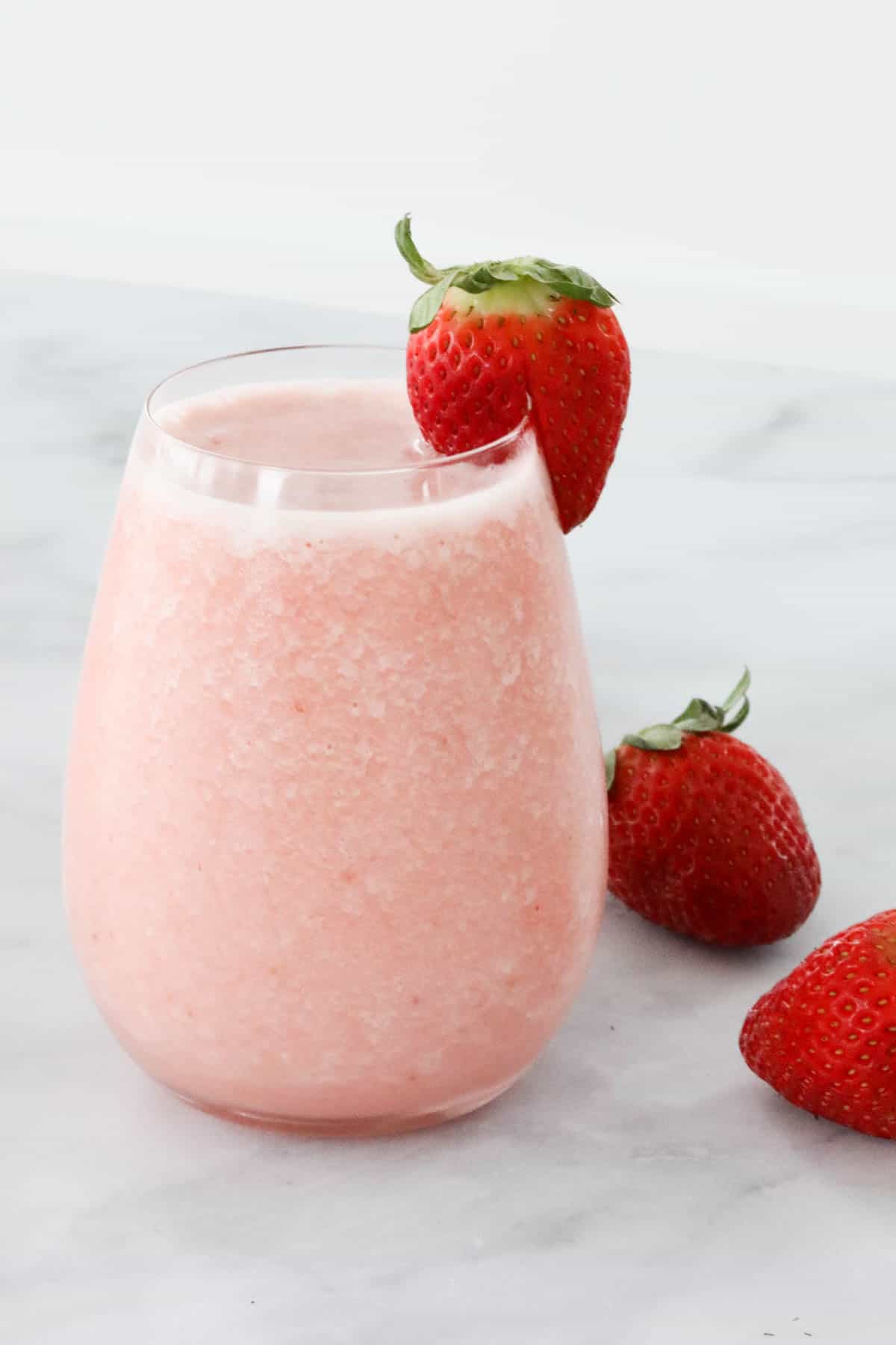 A strawberry colada in a glass with a fresh strawberry on top.