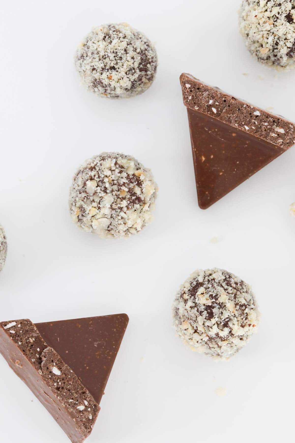 Chocolate balls coated in crushed hazelnuts and triangles of Toblerone chocolate on a white bench.