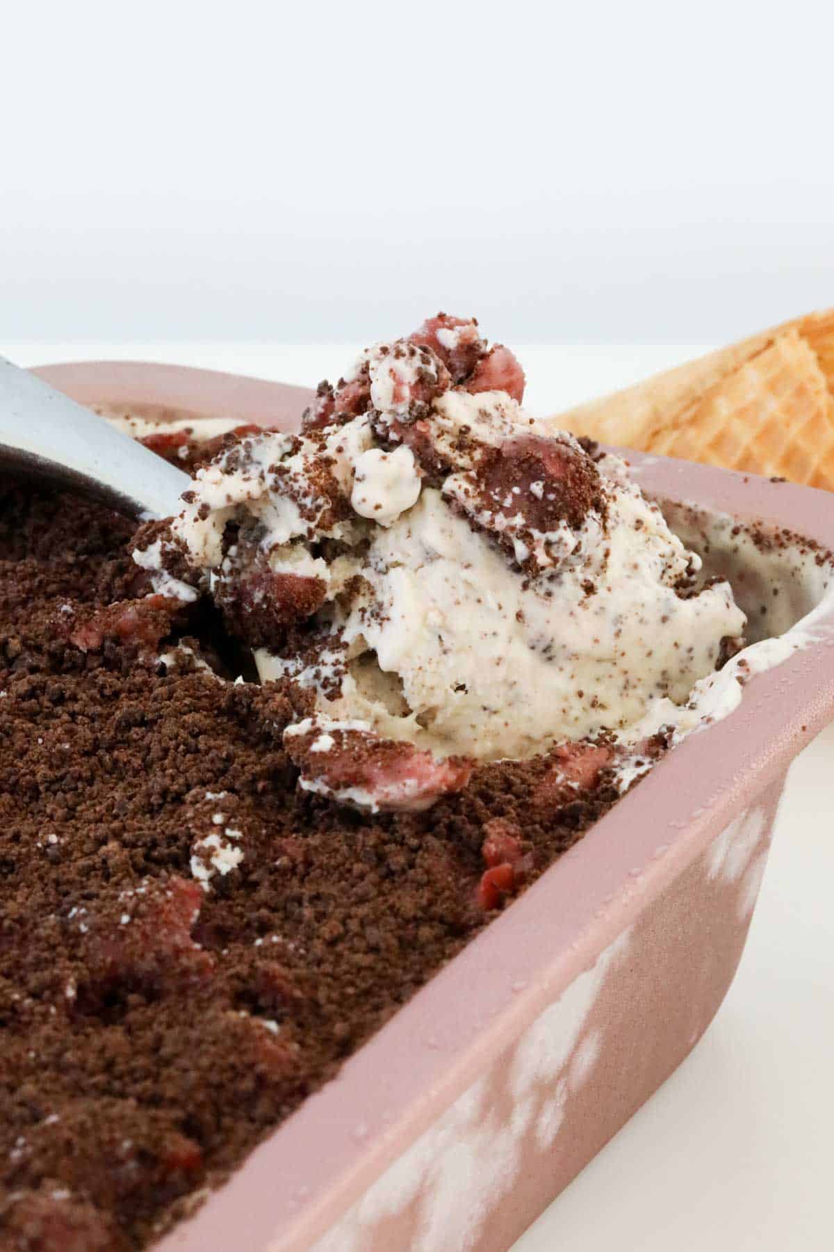 A spoon being dug into a loaf tin filled with chocolate and cherry ice cream.