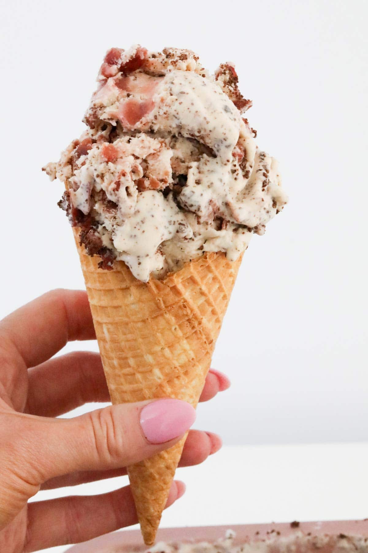 Black forest ice cream in a waffle cone being held up.