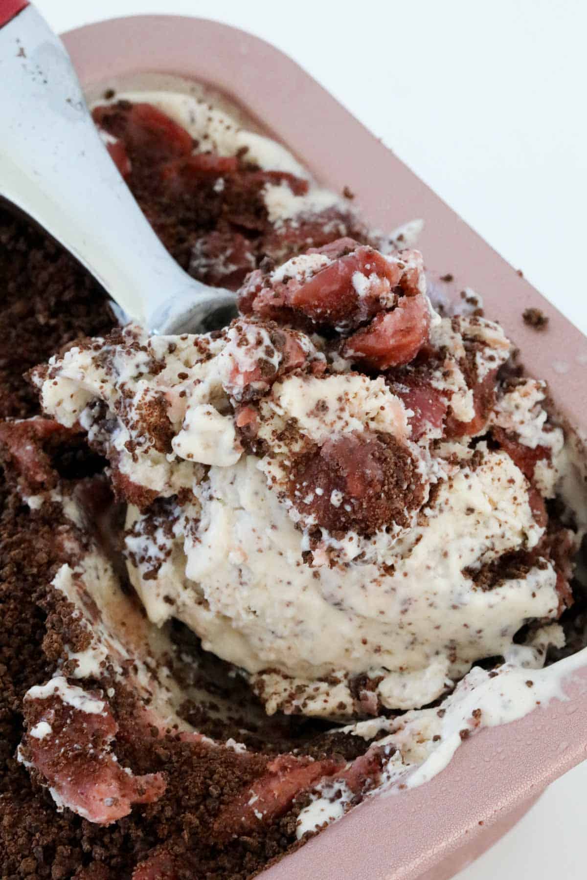 A close up of a spoonful of ice cream showing chunks of cherry and grated chocolate throughout.