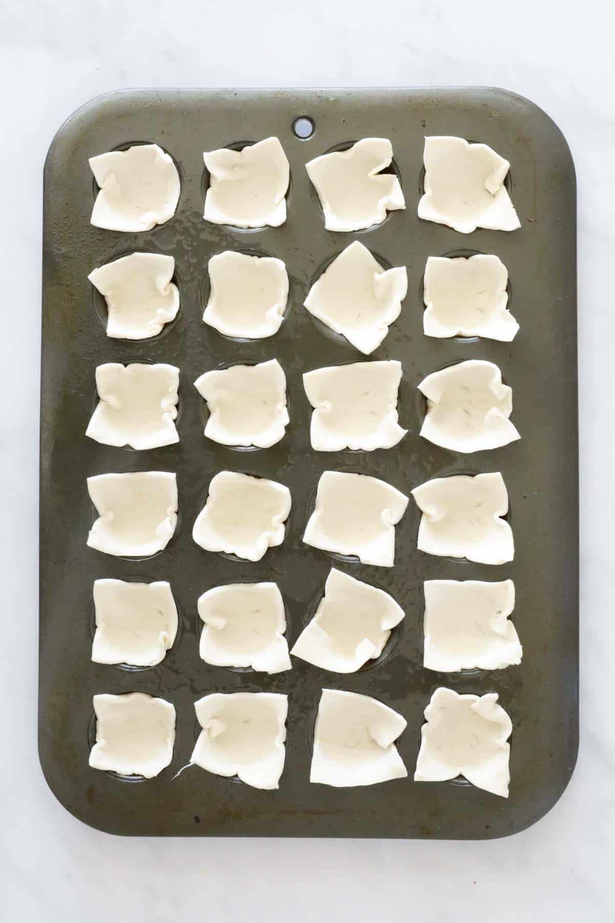 Puff pastry squares pressed into a mini muffin tray.