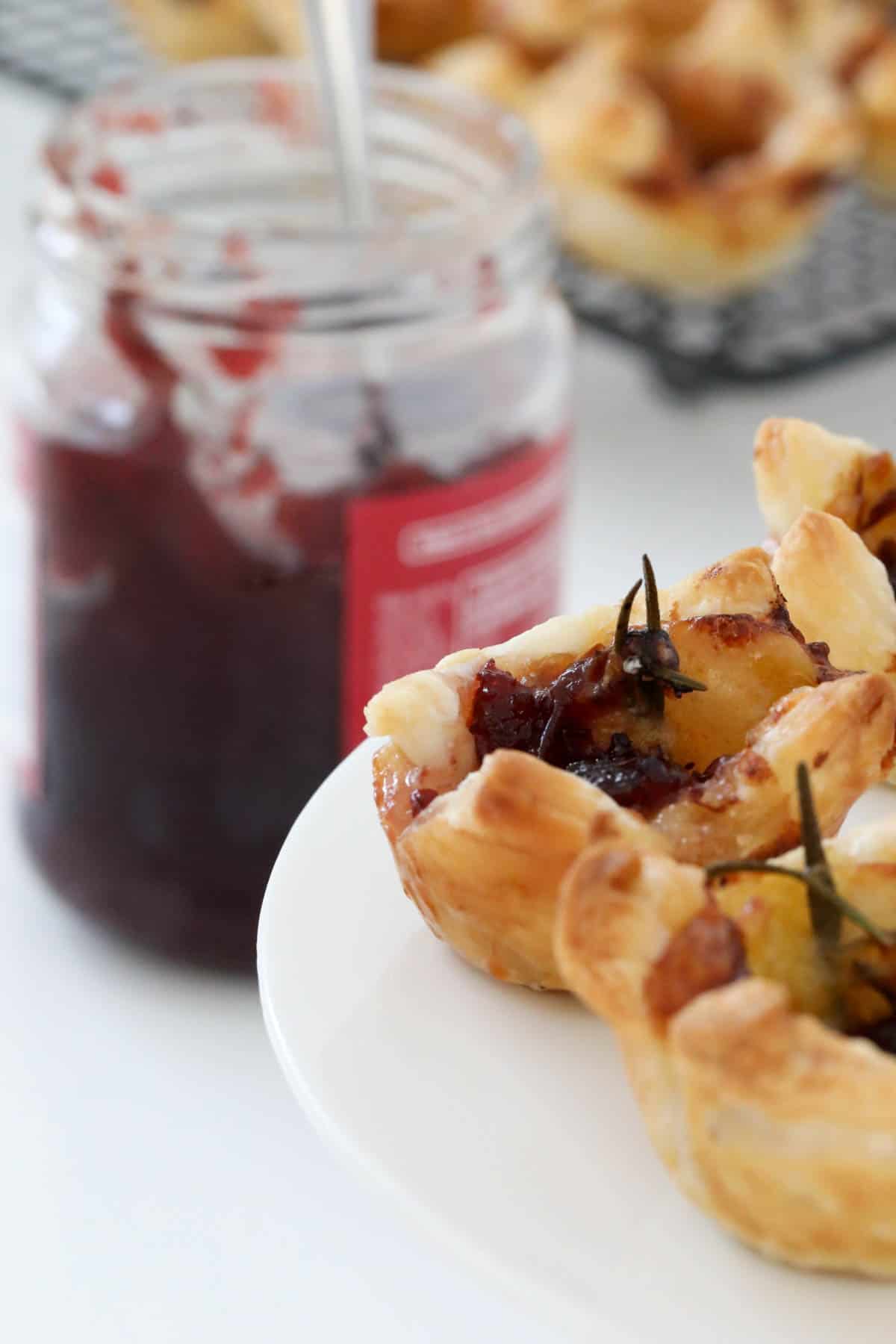 A jar of cranberry sauce behind a plate of puff pastry bites.