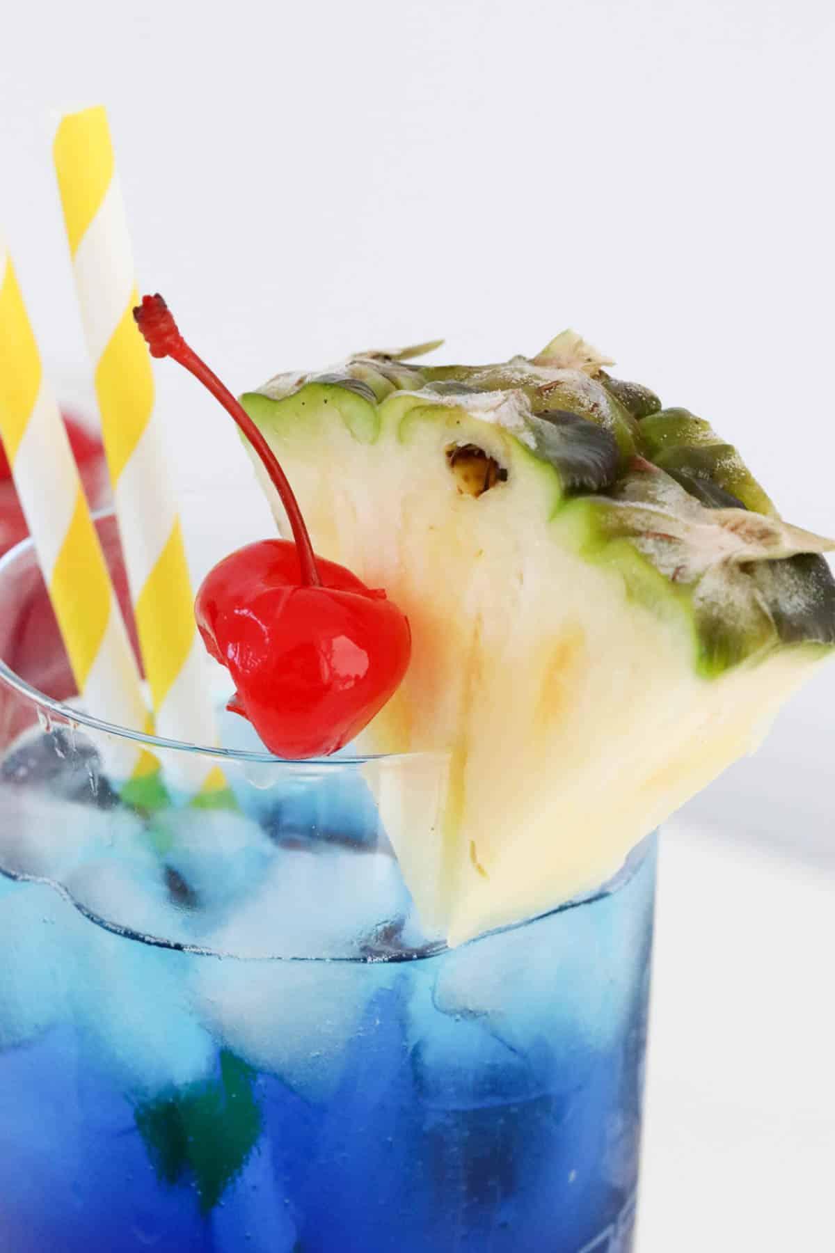 A close up shot of a cherry and pineapple in a glass with yellow straws.