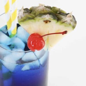 A cherry and a pineapple wedge on top of a glass filled with a blue cocktail.