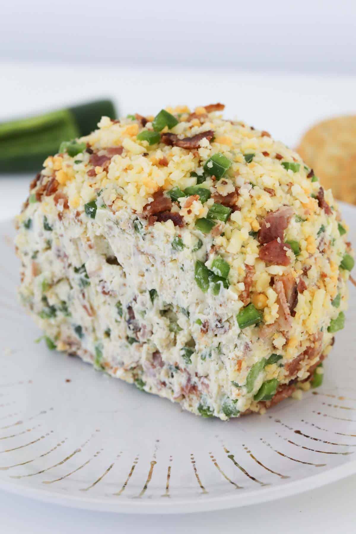 The jalapeño popper cheese ball on a plate with a slice cut out to show the texture.