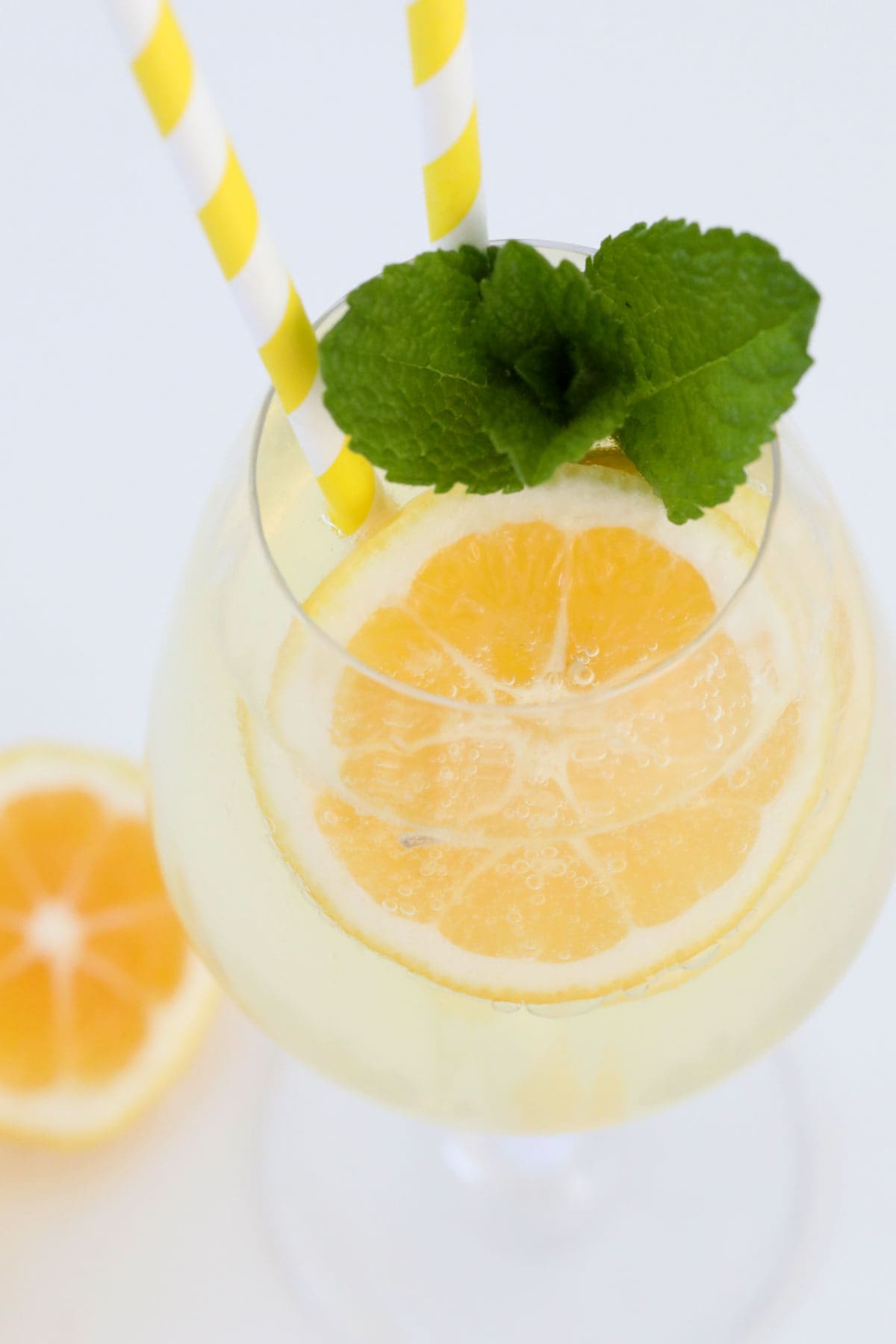 A glass of limoncello spritz served with fresh mint, lemon slices and two straws.