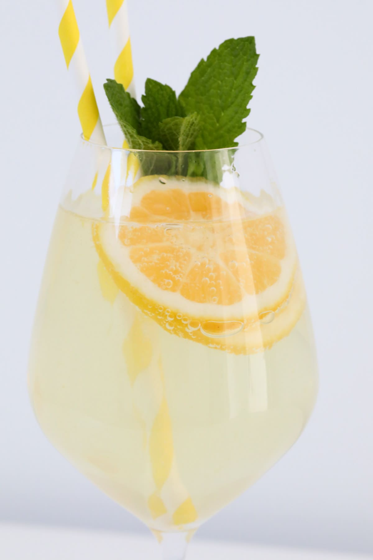 Side view of a glass of chilled limoncello spritz with slices of lemon added and a sprig of fresh mint.