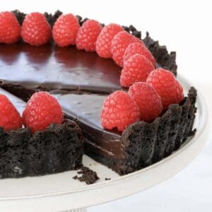 A slice of rich and decadent chocolate ganache tart with raspberries on top.