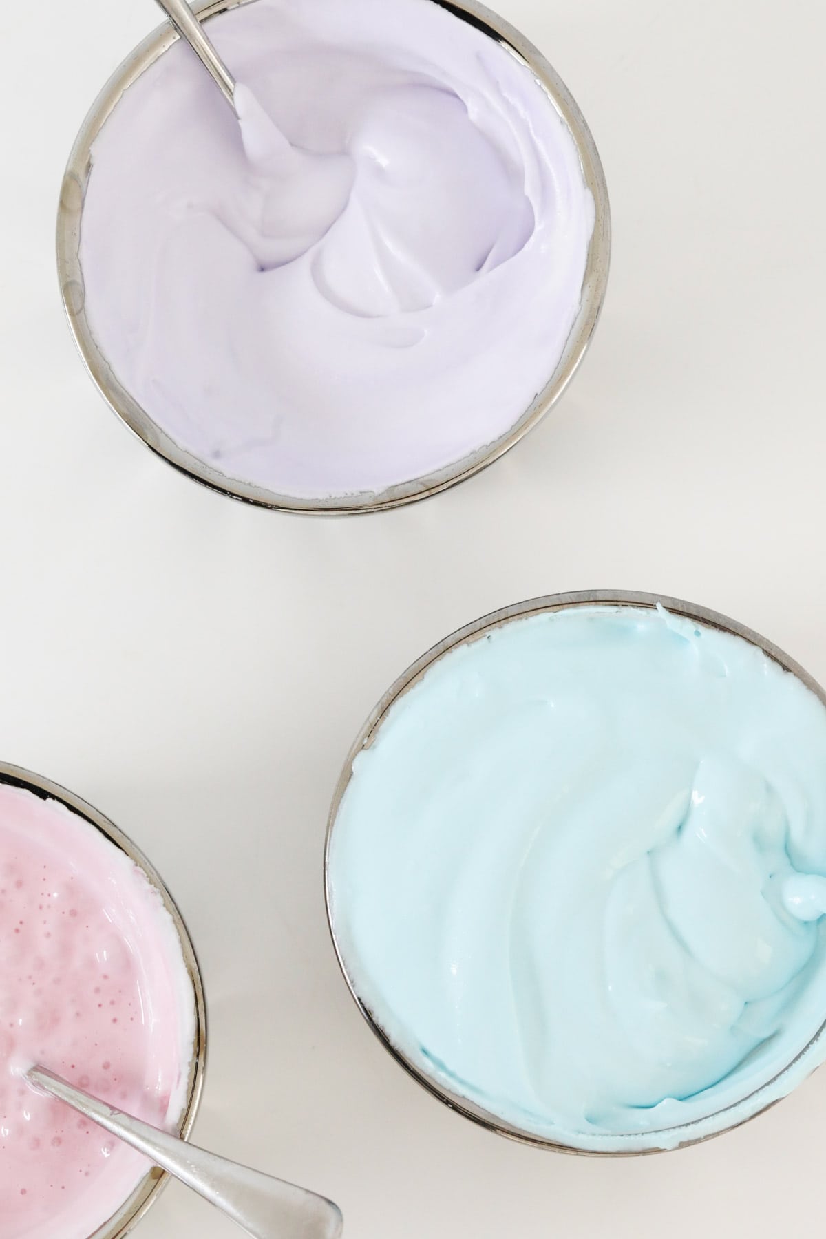 Three bowls of royal icing: one purple, one blue and one pink.