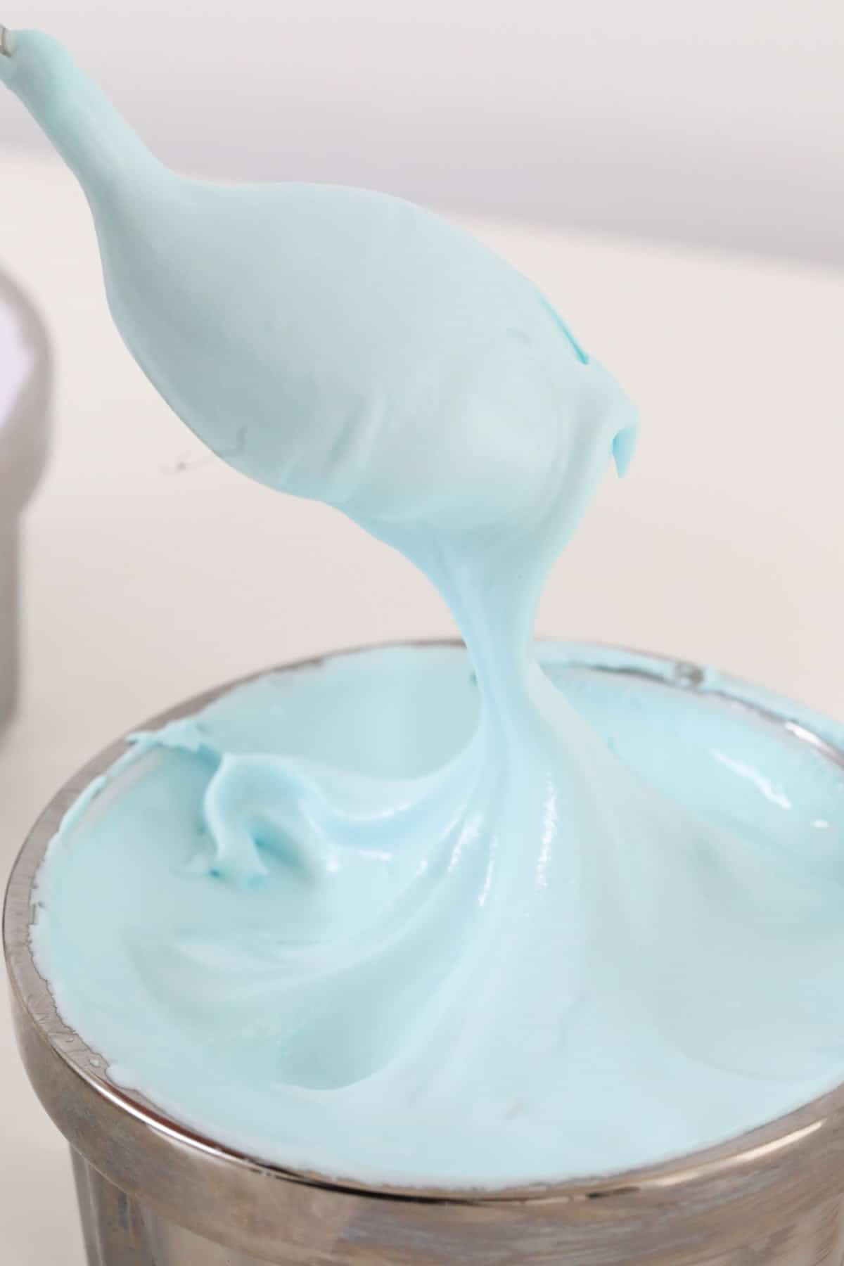 A spoon holding up some blue royal icing.
