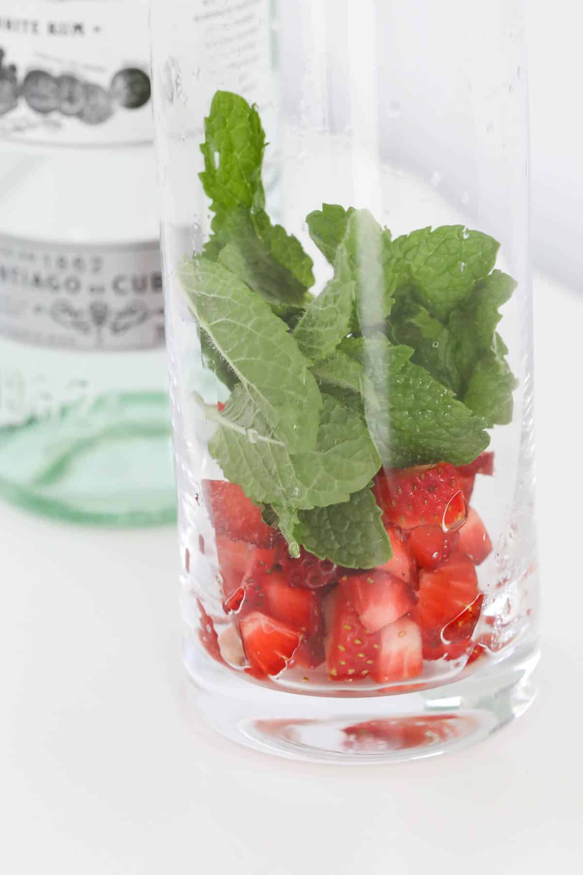 Diced strawberries and mint leaves added to a glass.