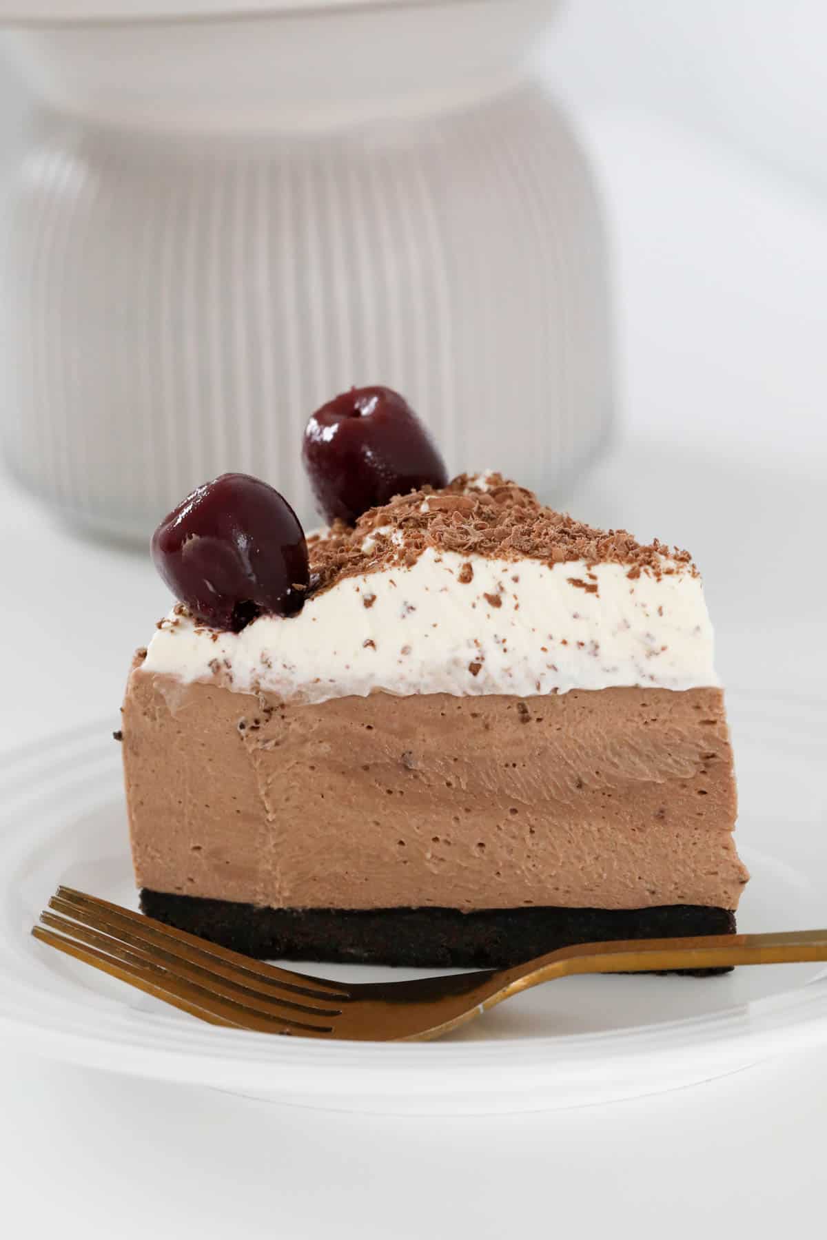 Side view of chocolate cheesecake with cream, black cherries and chocolate on top.