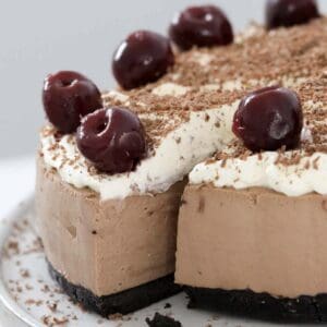 A slice of chocolate cheesecake topped with whipped cream, chocolate and cherries being removed from the cheesecake.