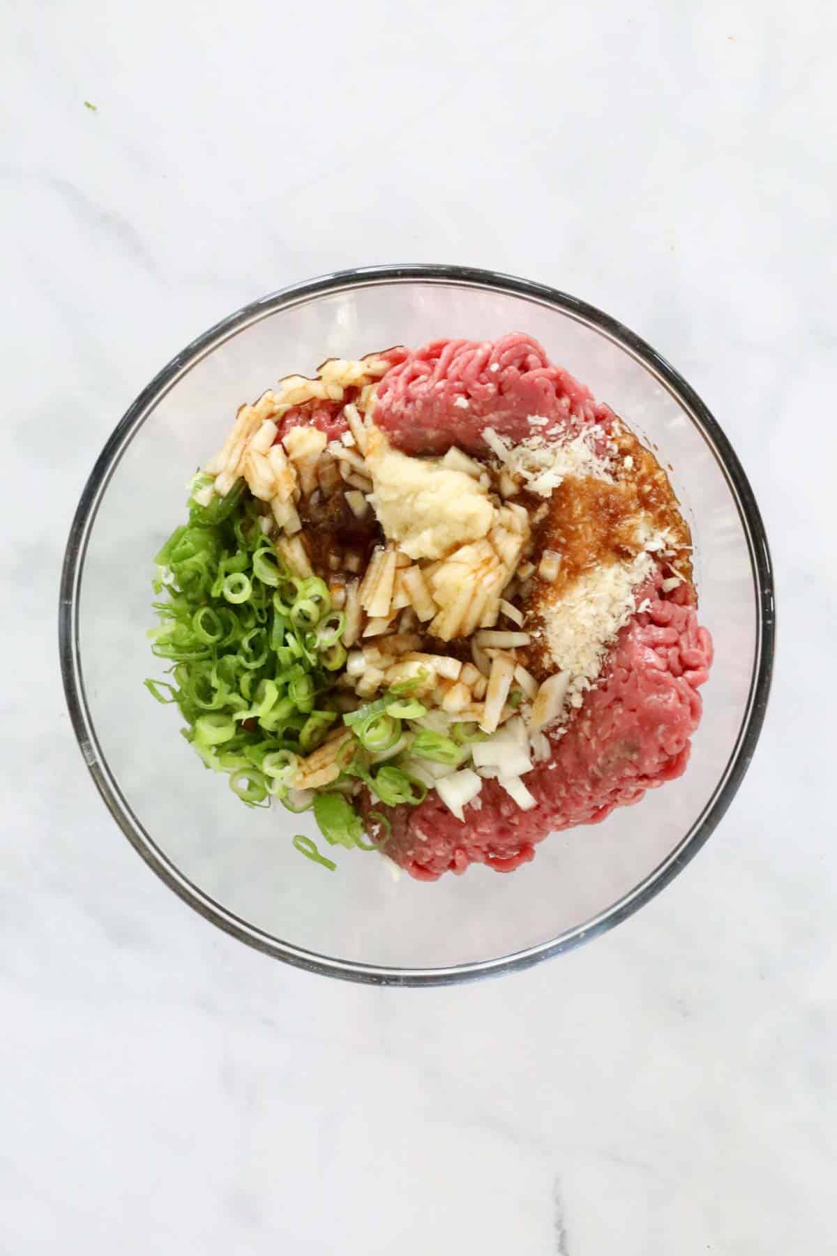 The minced beef, spring onions, ginger, spicy sauce, and breadcrumbs in a large mixing bowl.