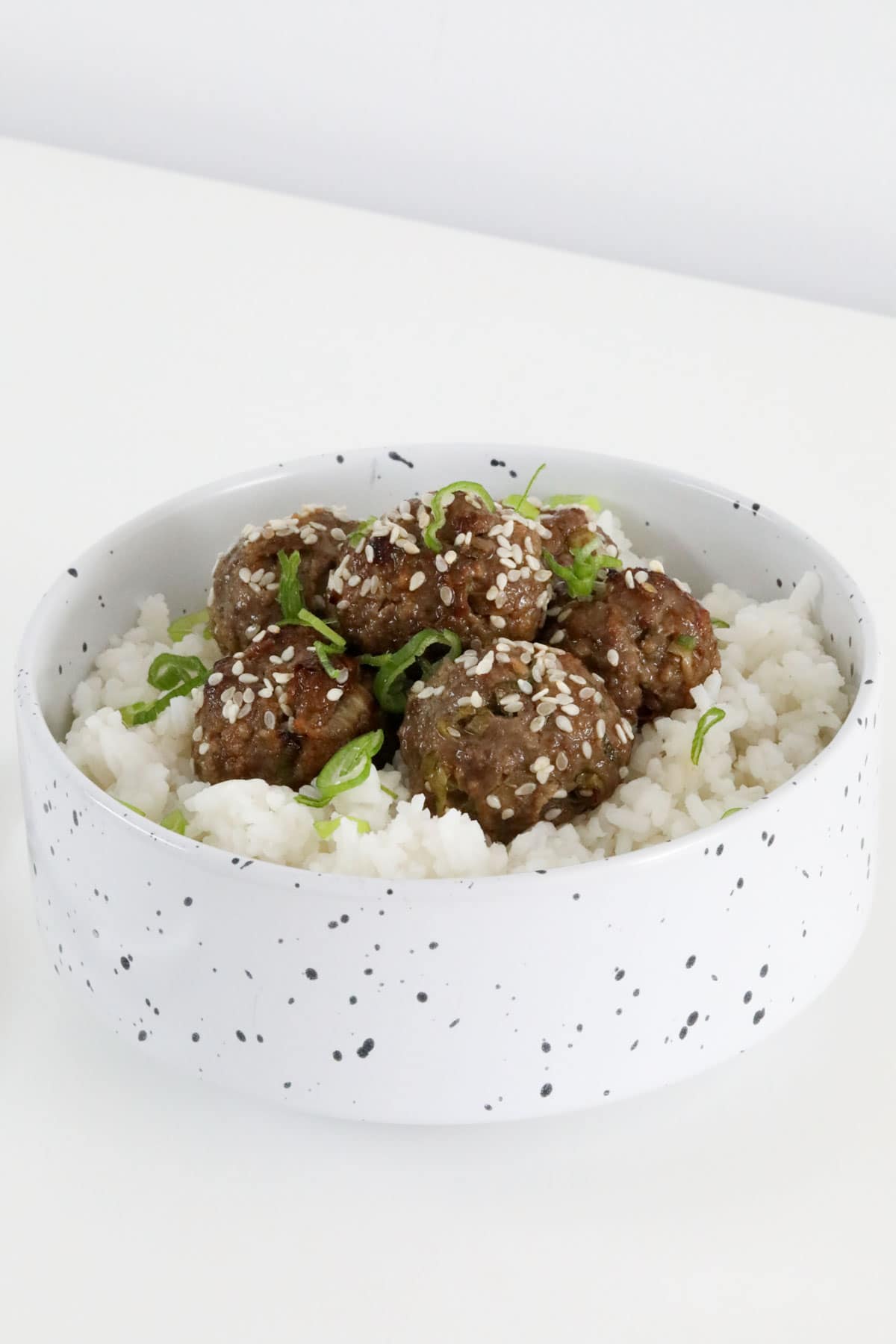 A white speckled bowl filled with rice topped with beef meatballs.