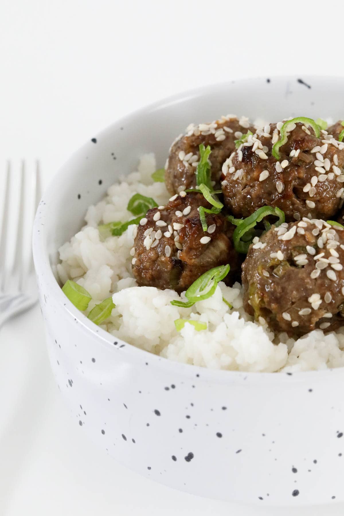 A bowl of meatballs and rice topped with sesame seeds and spring onions.