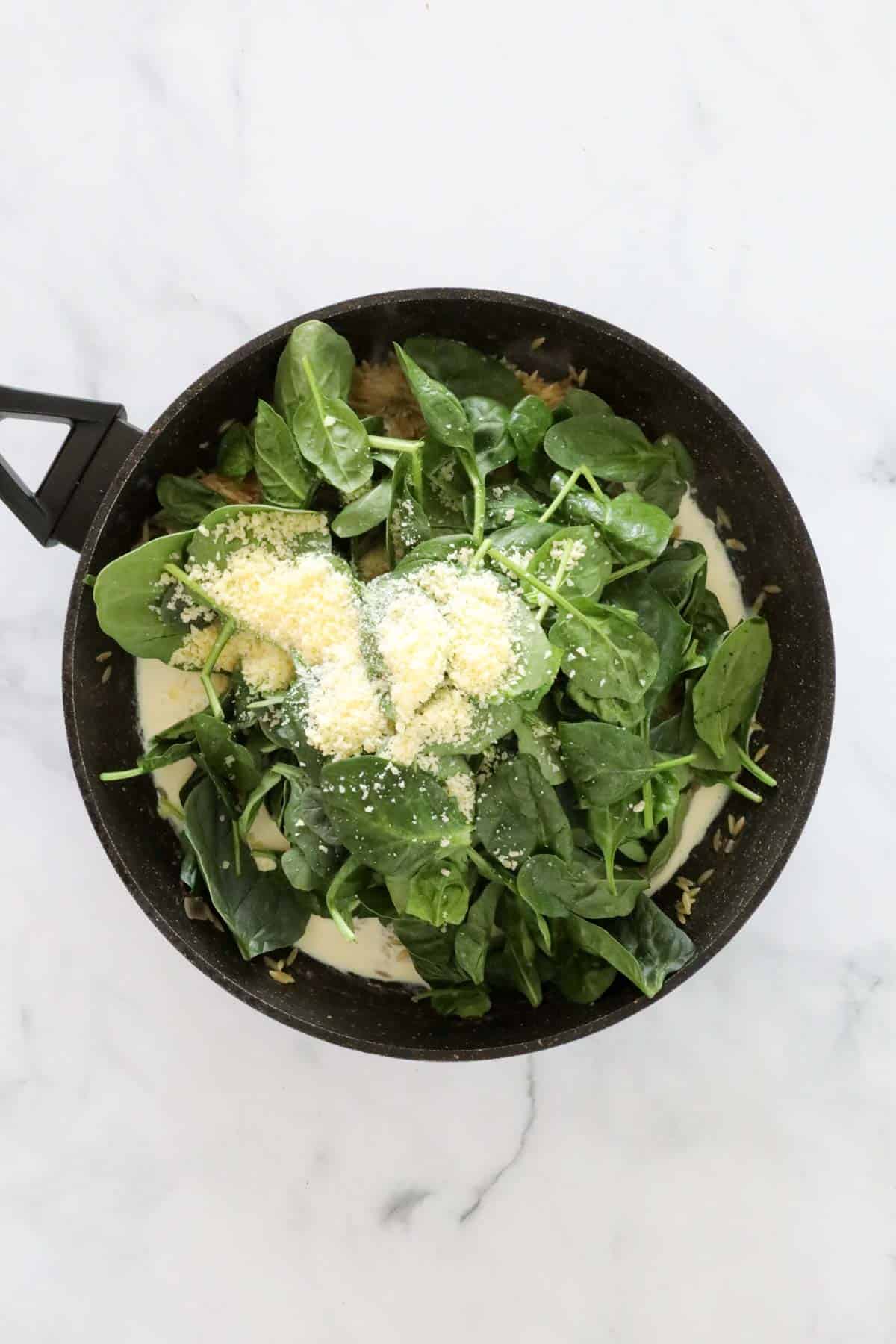 Fresh spinach leaves, lemon juice, parmesan and cream added to frying pan of cooked risoni.