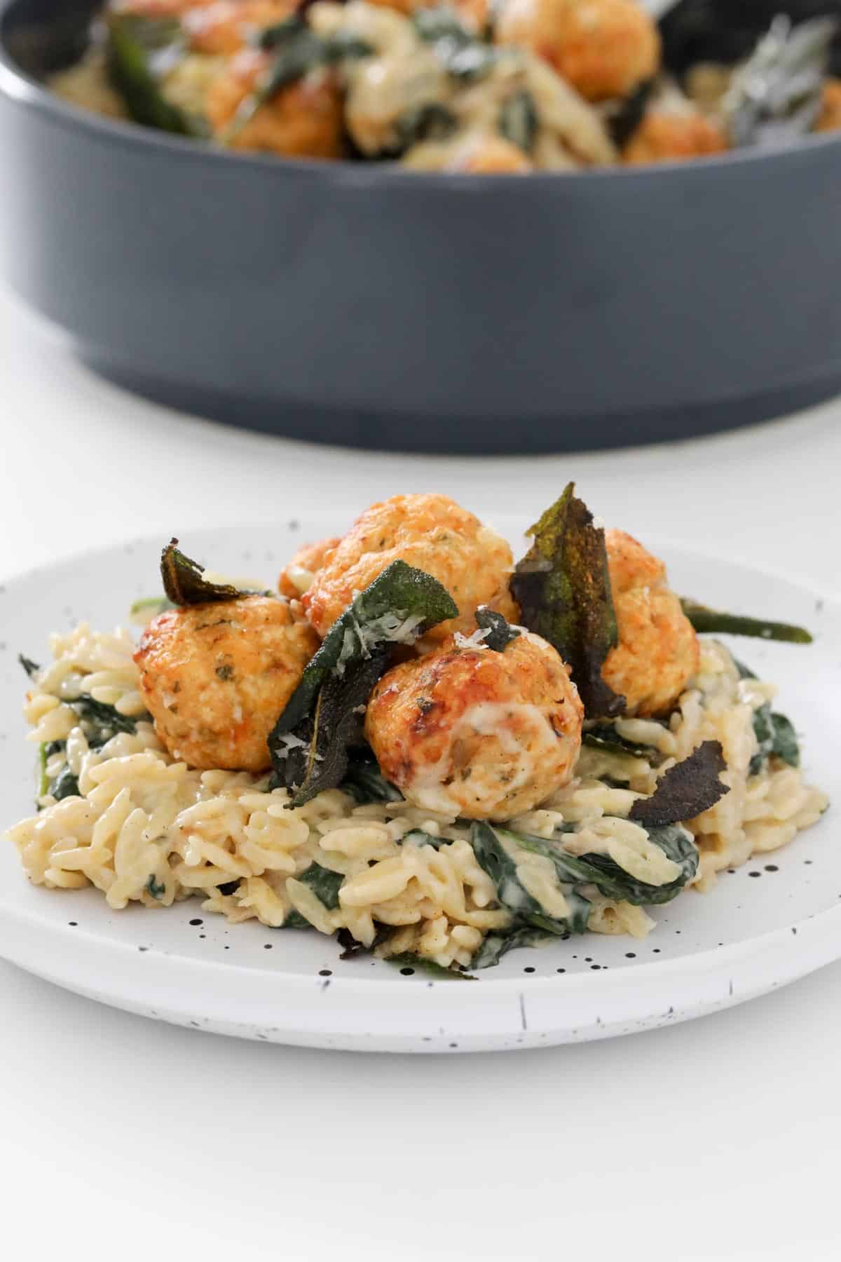 A plate with a serve of golden chicken meatballs with risoni and crispy fried sage leaves sprinkled on top.