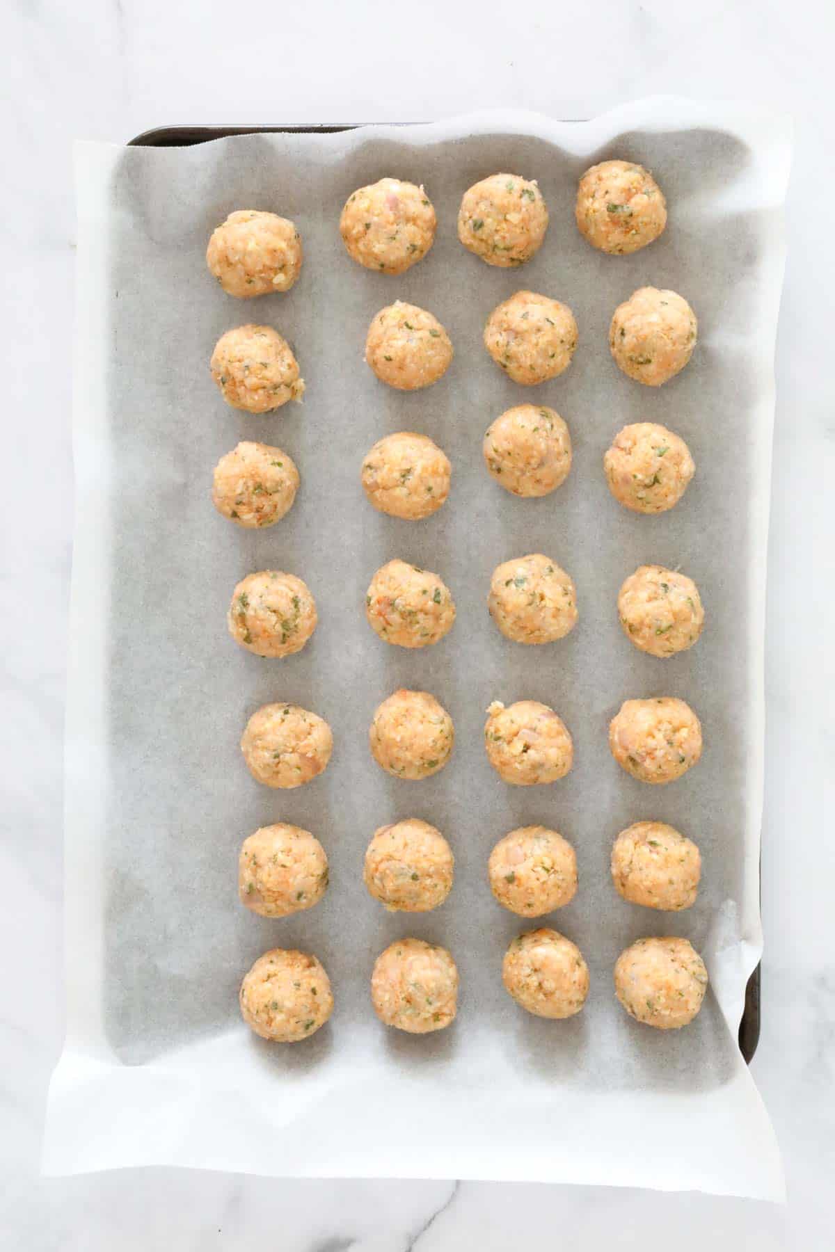 Small round meatballs on baking paper on a baking tray.