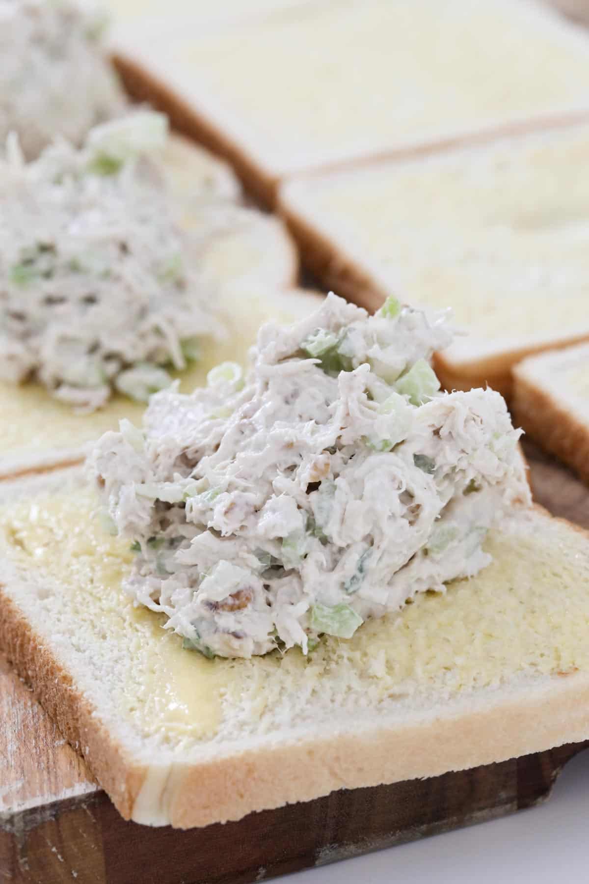 A spoonful of the creamy shredded chicken filling on a slice of buttered white bread.