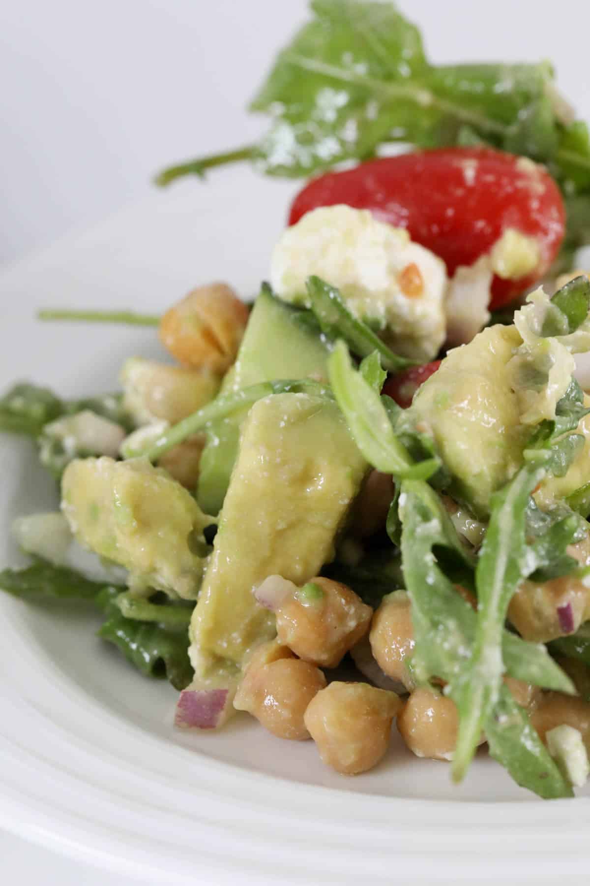 A serving of chickpea salad with avocado and rocket on a white serving plate.