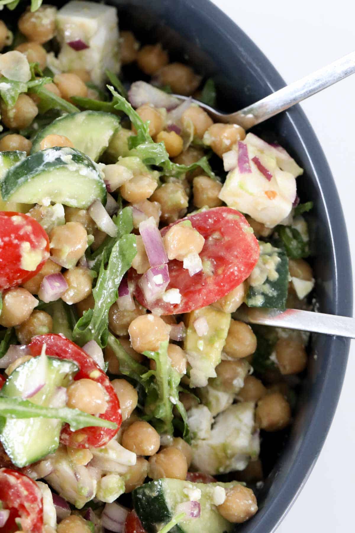 Chickpea and avocado salad in a serving bowl with salad servers.