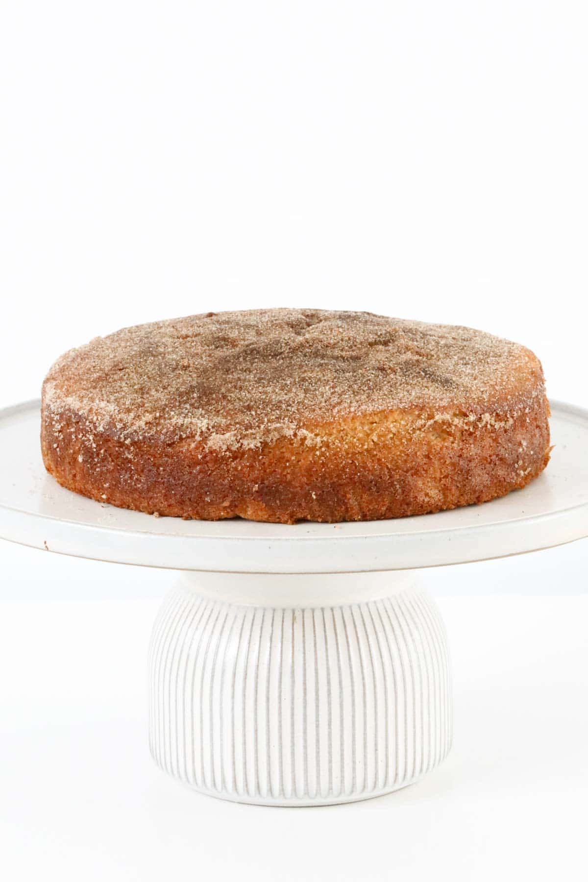 A baked cinnamon tea cake on a white cake platter.