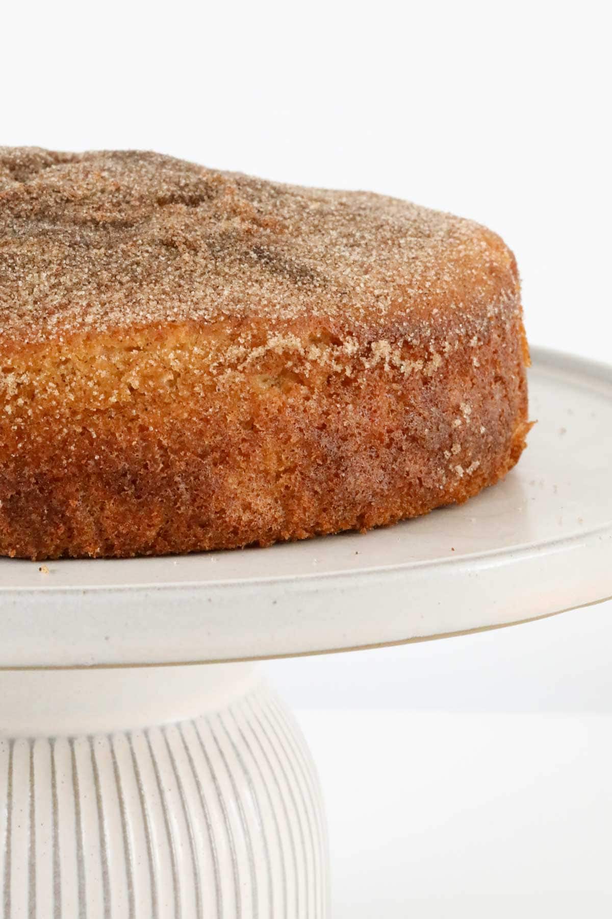 A tea cake with a cinnamon and sugar topping on a white cake stand.