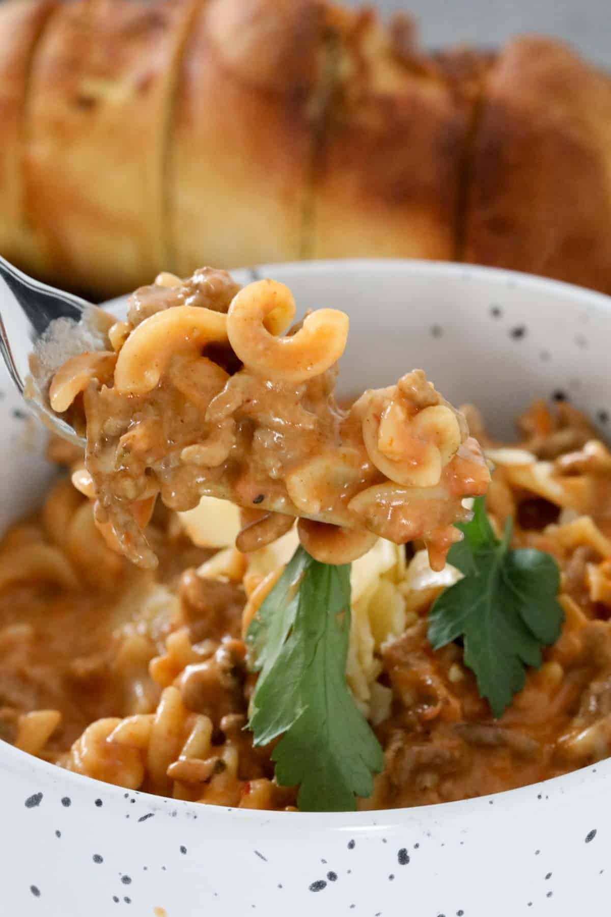 A forkful of creamy pasta and meat, held above a bowl.