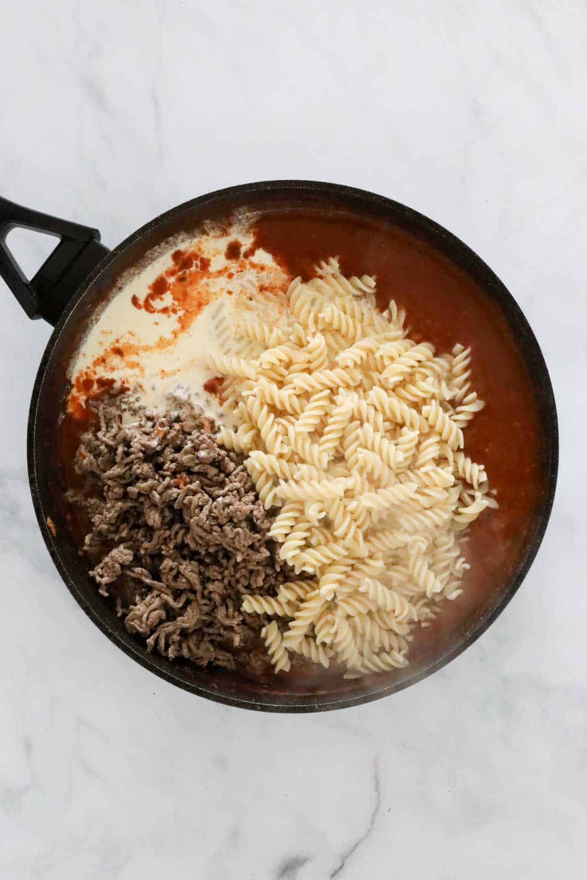 Browned mince, cooked spirals and cream added to the tomato sauce in the pan.