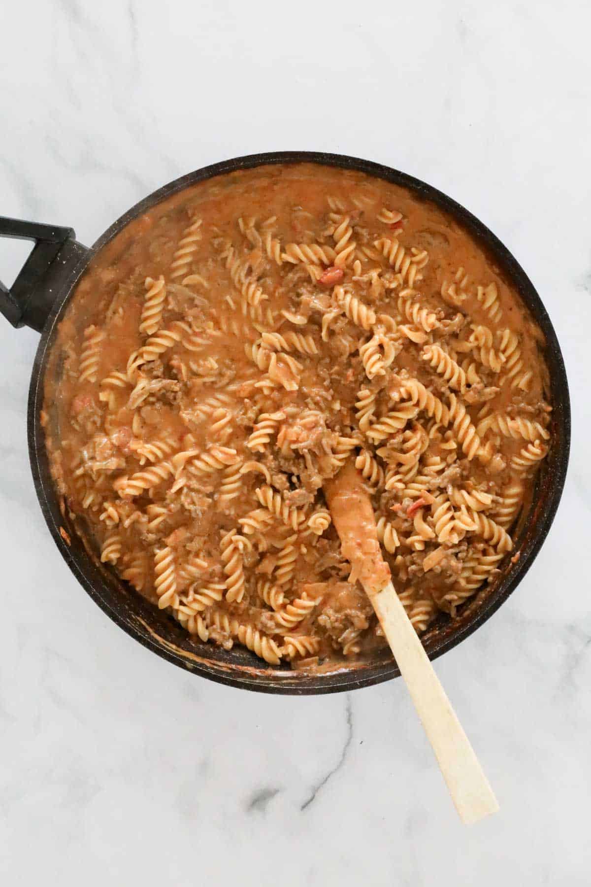 The creamy mixed beef and pasta in the pan with a wooden spoon.