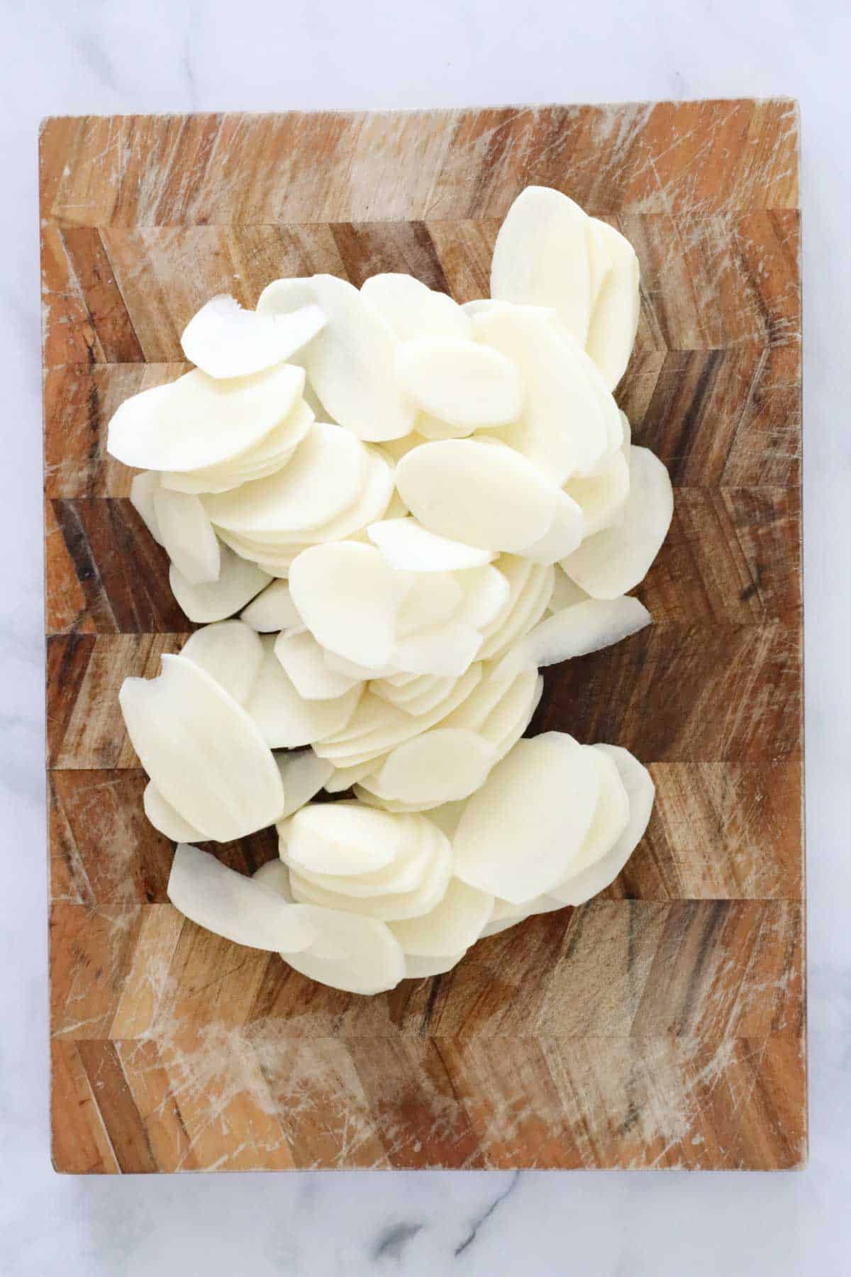 A pile of peeled and finely sliced potatoes on a wooden board.