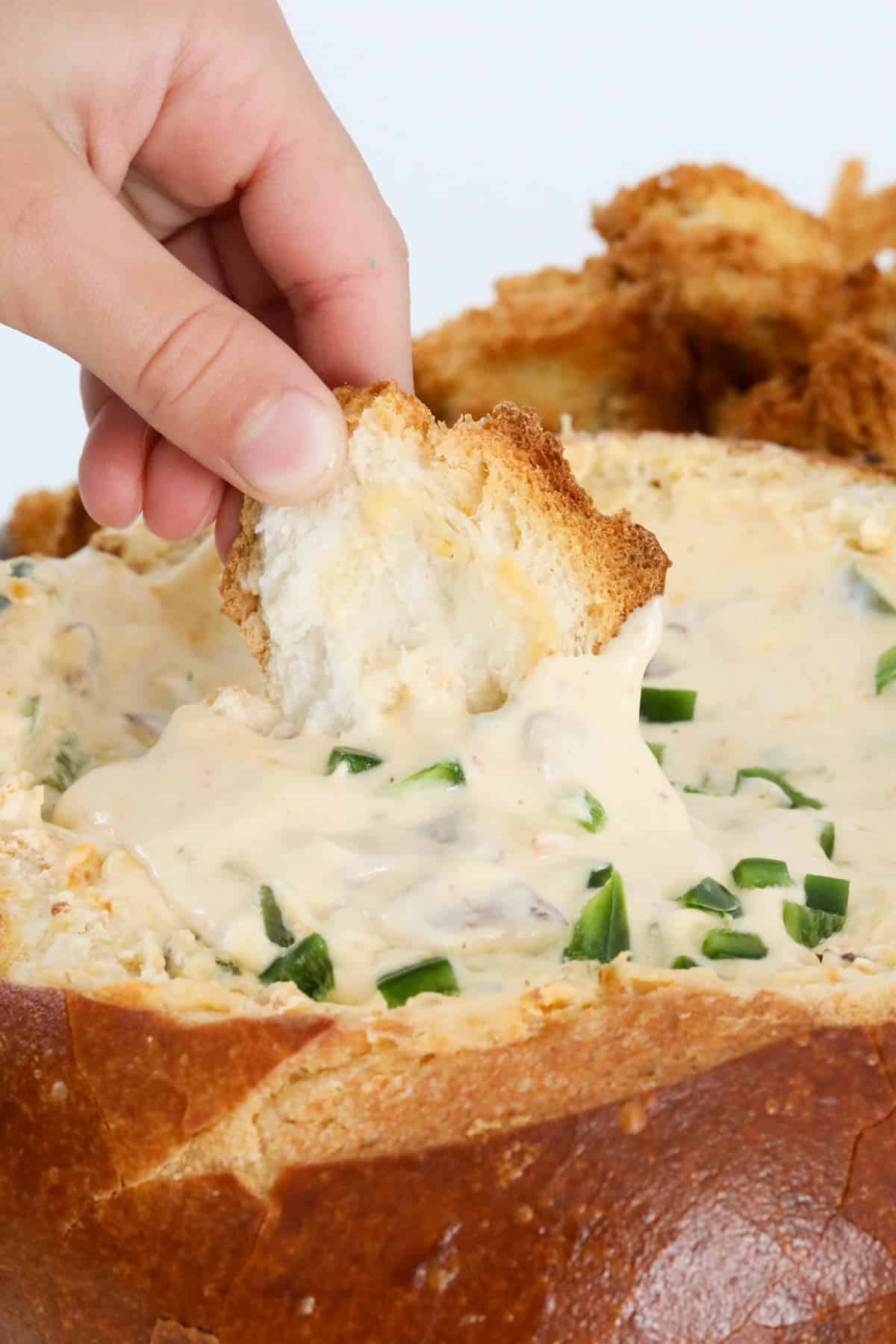 A hand dipping a pieces of baked bread into Jalapeño popper cob loaf.