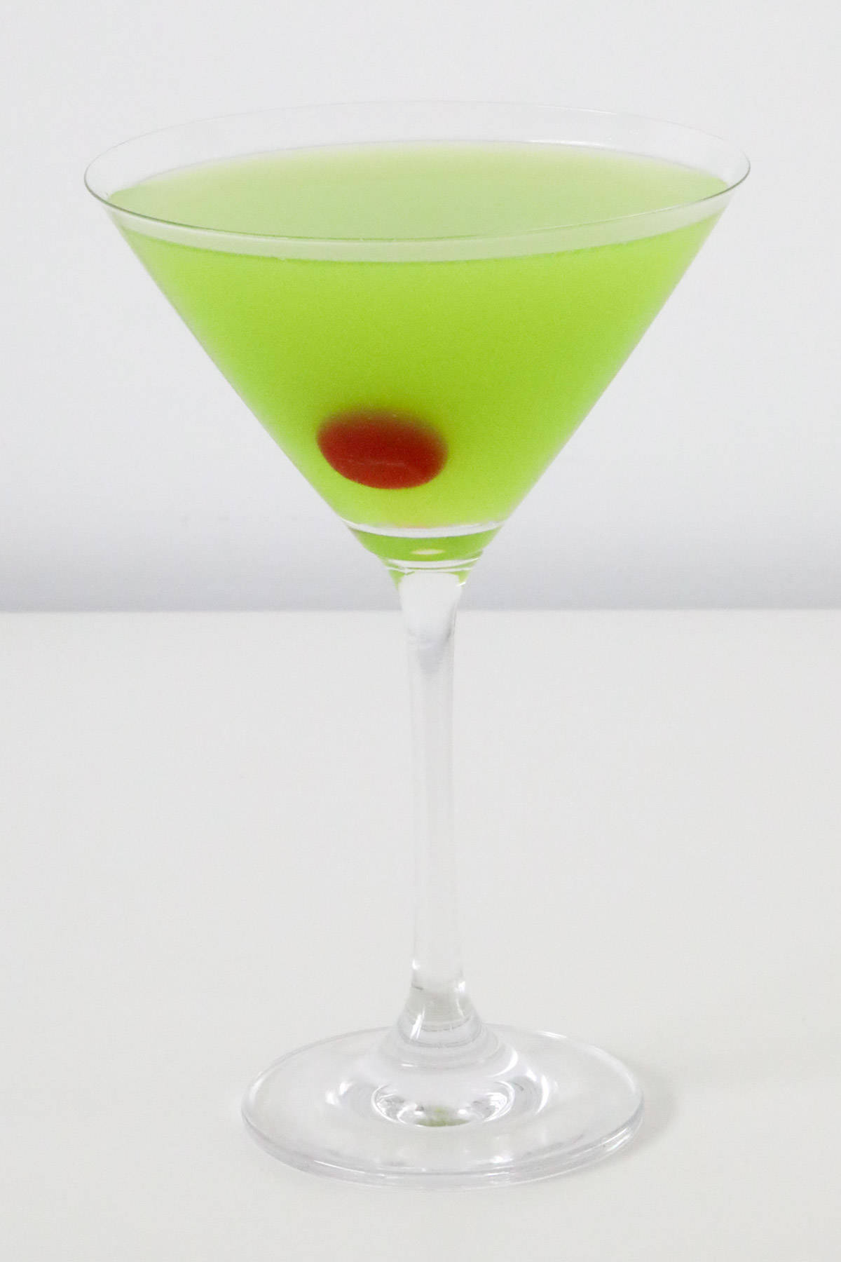 A martini glass filled with a lime green Japanese slipper cocktail and a maraschino cherry.