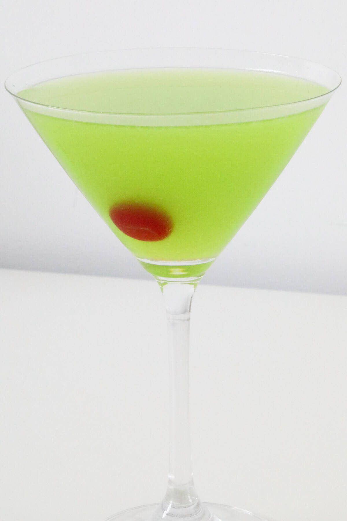 An icy cold pale green cocktail with a cherry, in a martini glass.