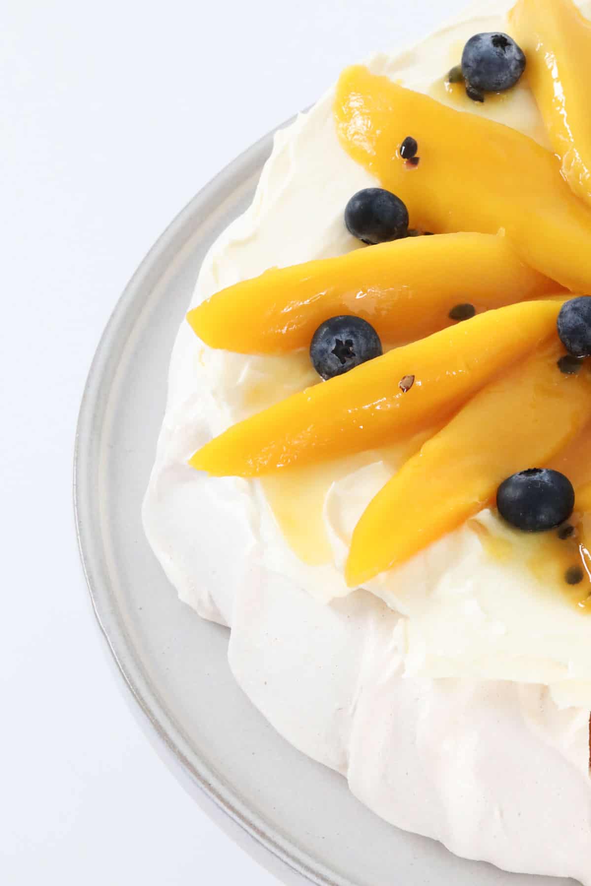 The pavlova decorated with whipped cream, mango slices and fresh blueberries..