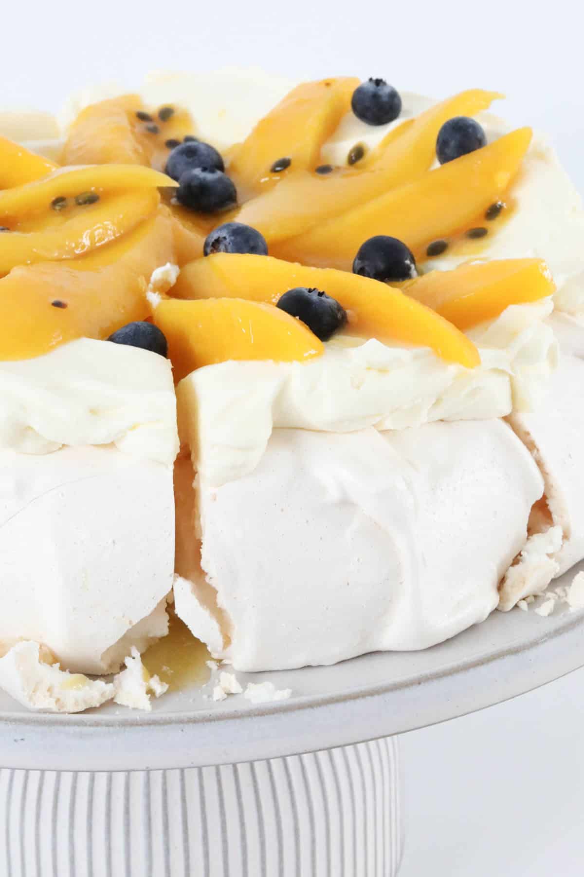 Passionfruit and mango pavlova on a cake stand with a slice cut ready to serve.