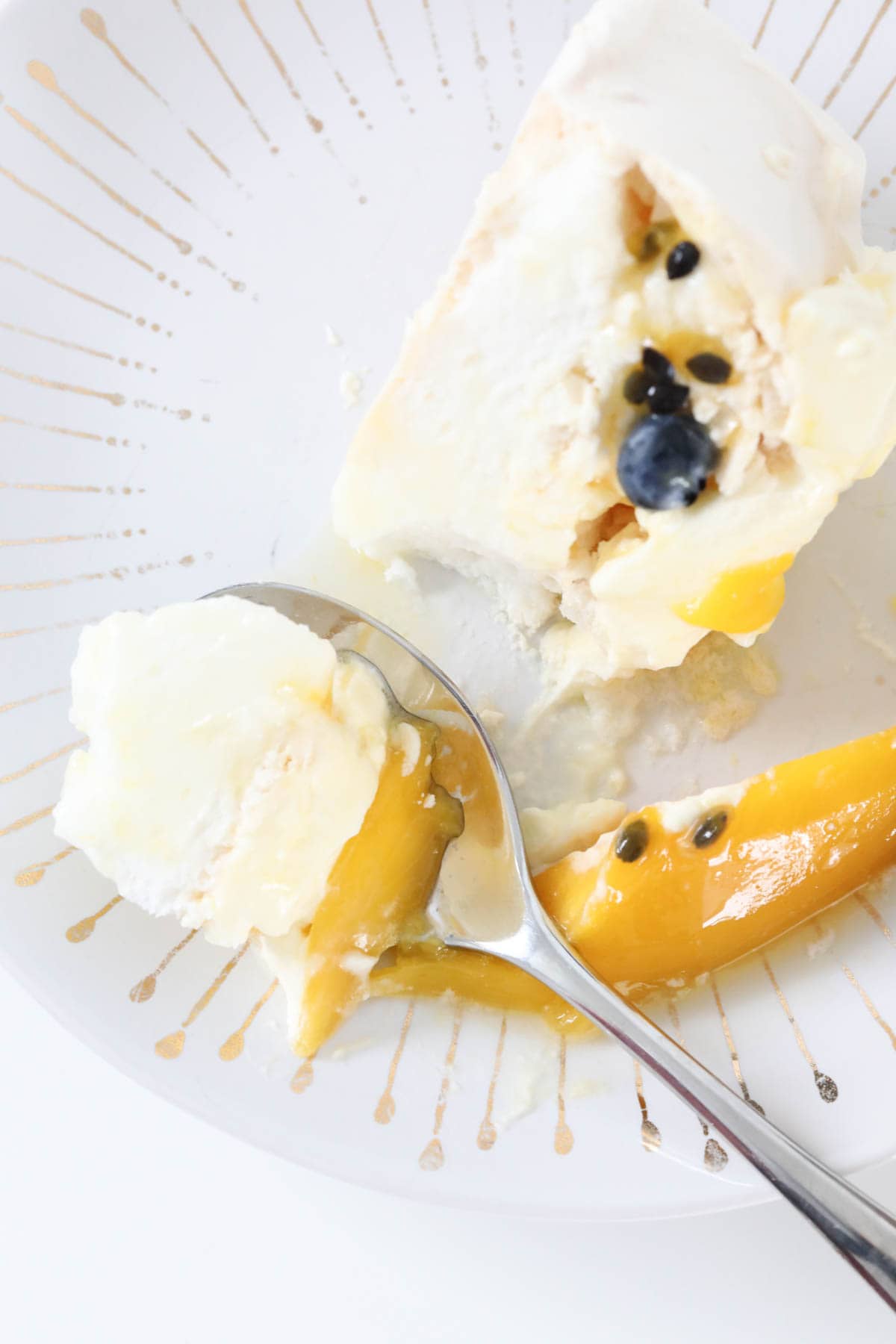 A slice of passionfruit mango pavlova on a plate with a spoonful taken out.