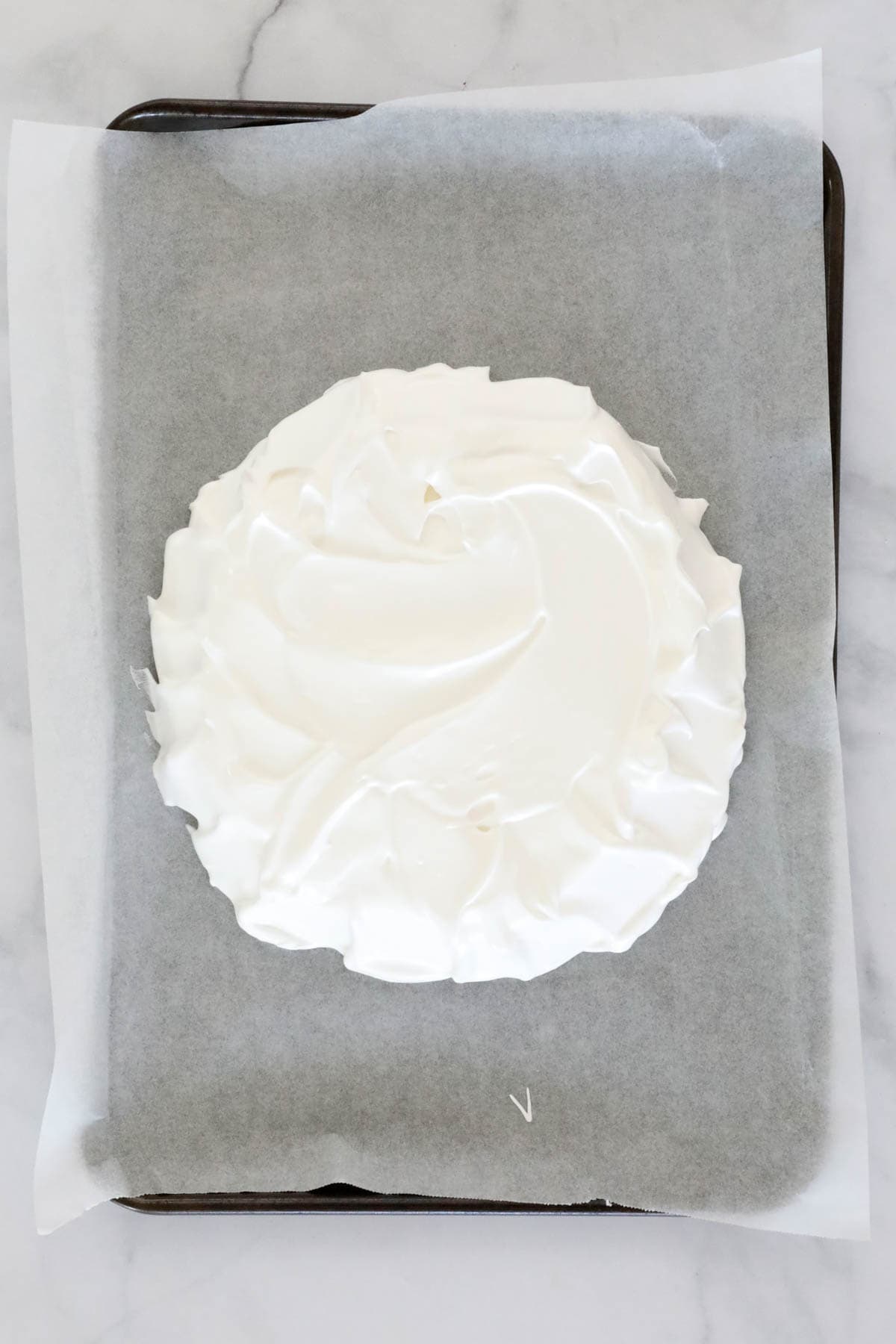 The pavlova mixture spooned onto a paper lined tray and flattened out into a dome-shape.