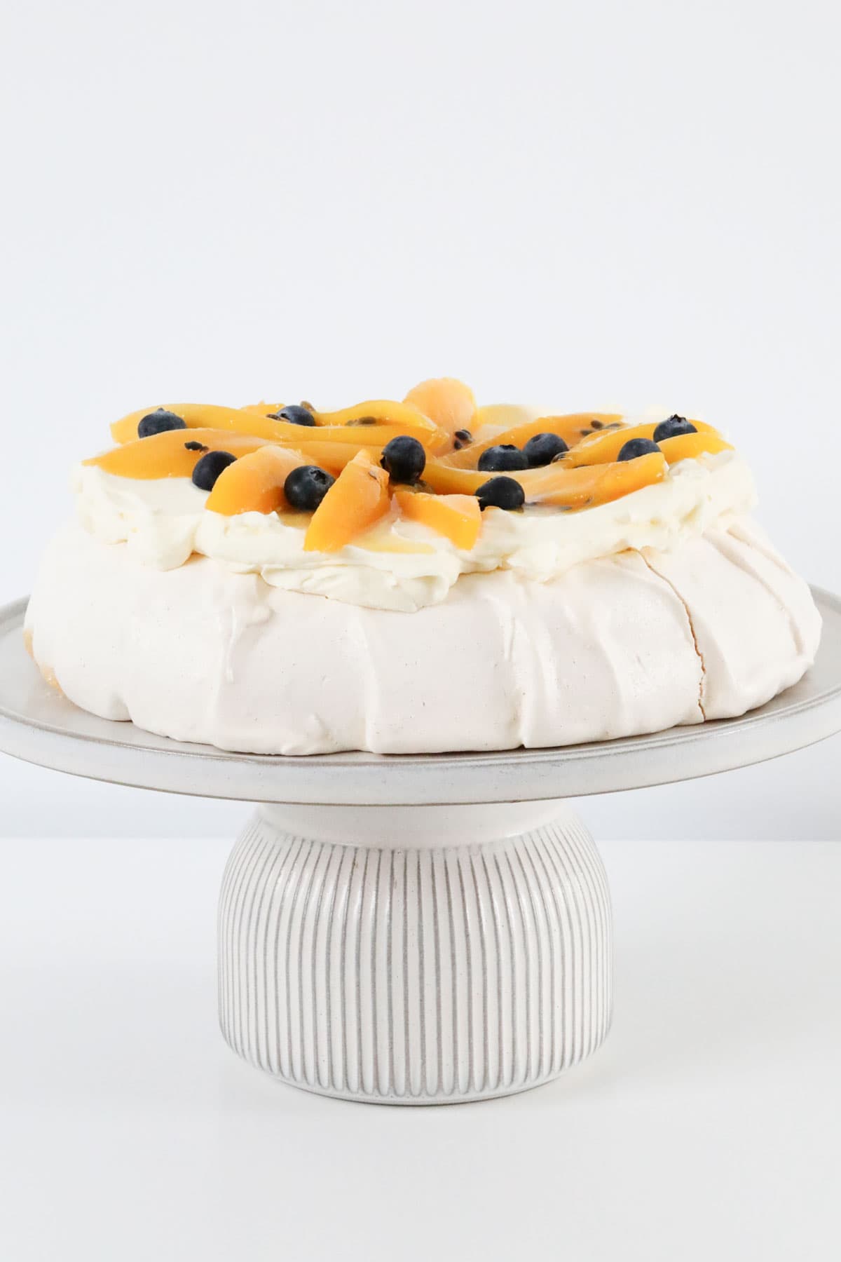 A pavlova decorated with mango slices, served on a cake stand.