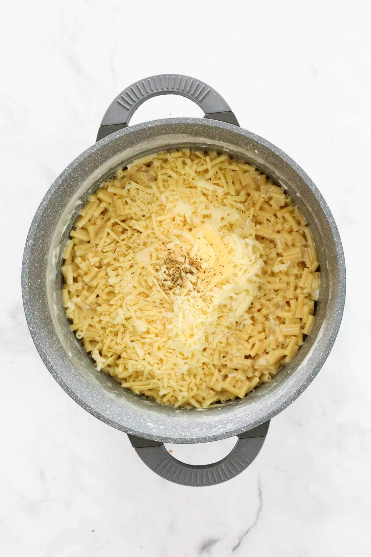 Grated cheeses and seasonings added to pasta in a pot.