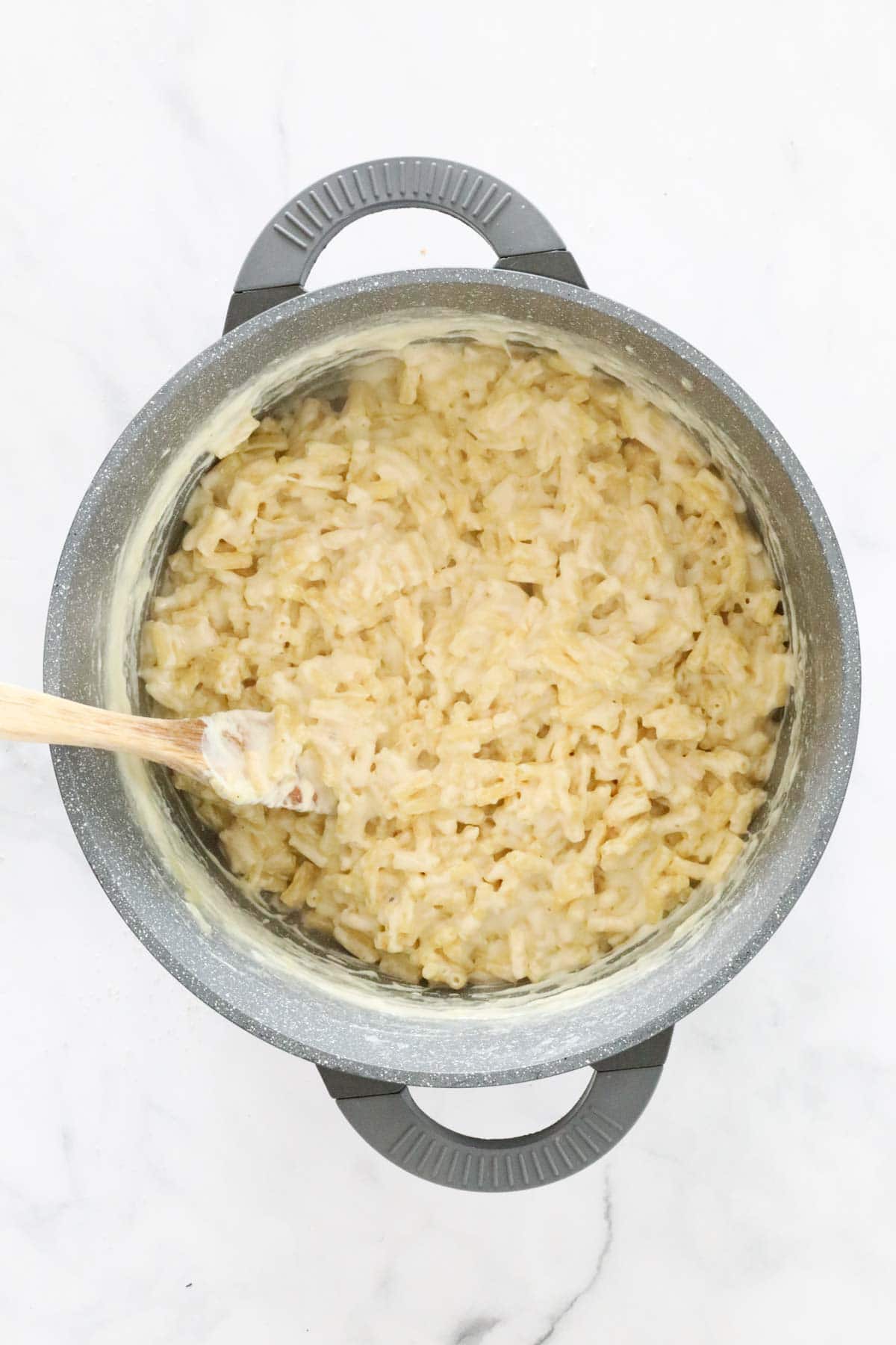 Cooked mac and cheese being stirred with a wooden spoon in the pot.