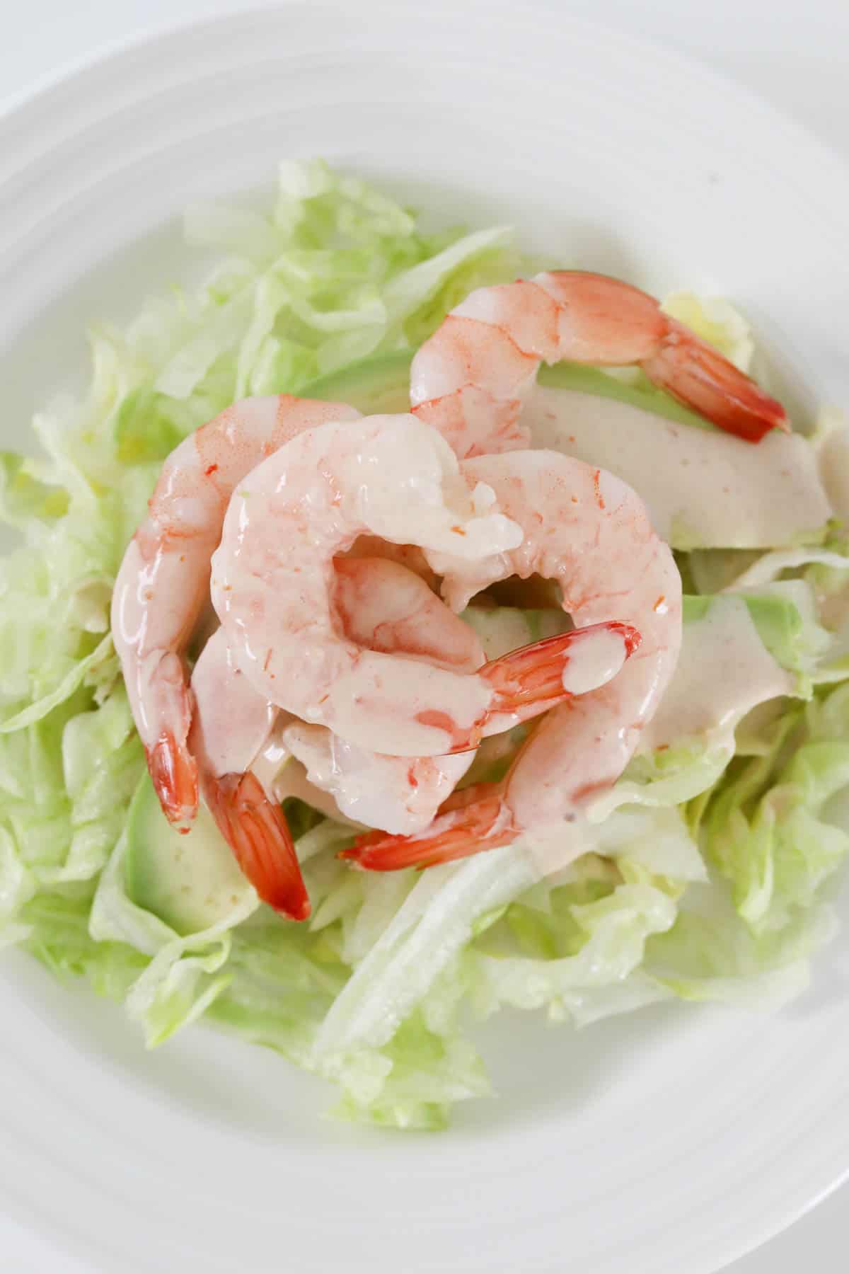 Overhead view of the prawn cocktail salad on a white serving plate drizzled with cocktail sauce.